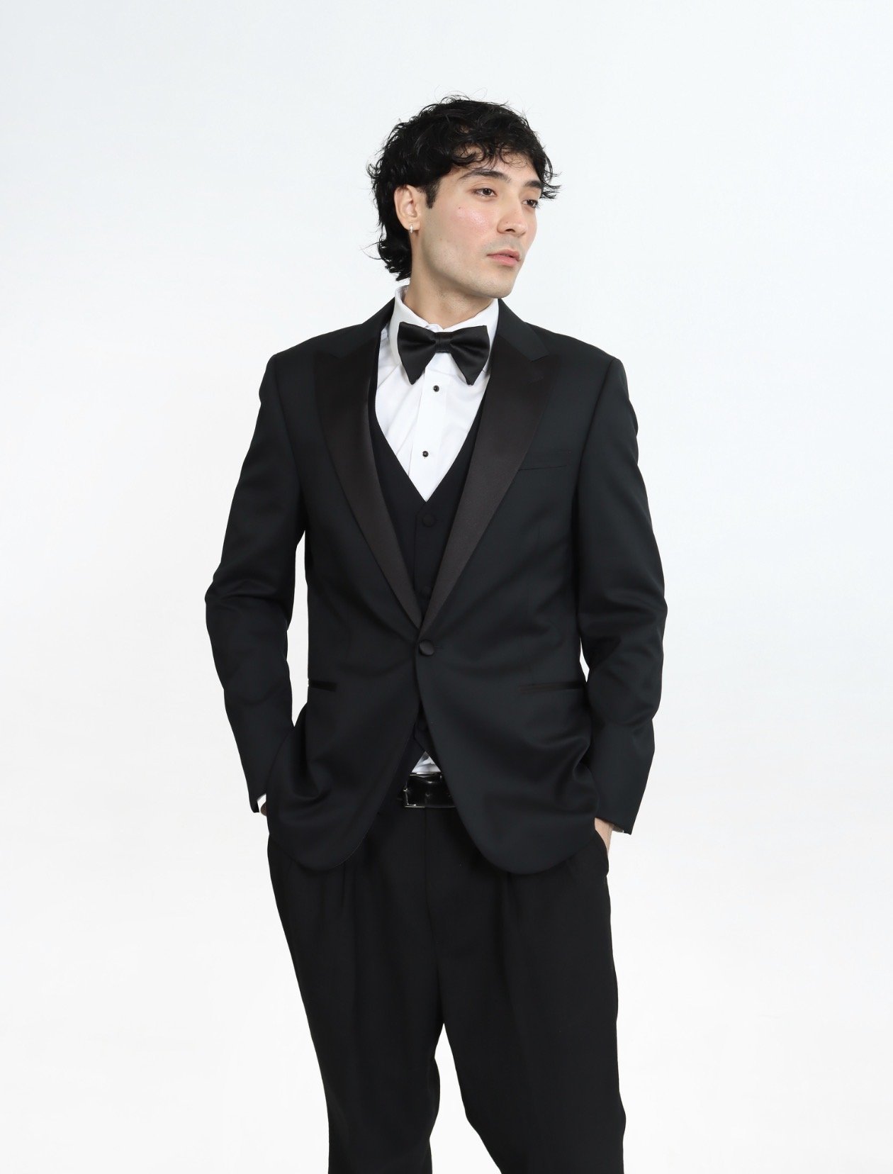 A man wearing a black tuxedo with a white shirt and black bow tie, standing against a plain white background.