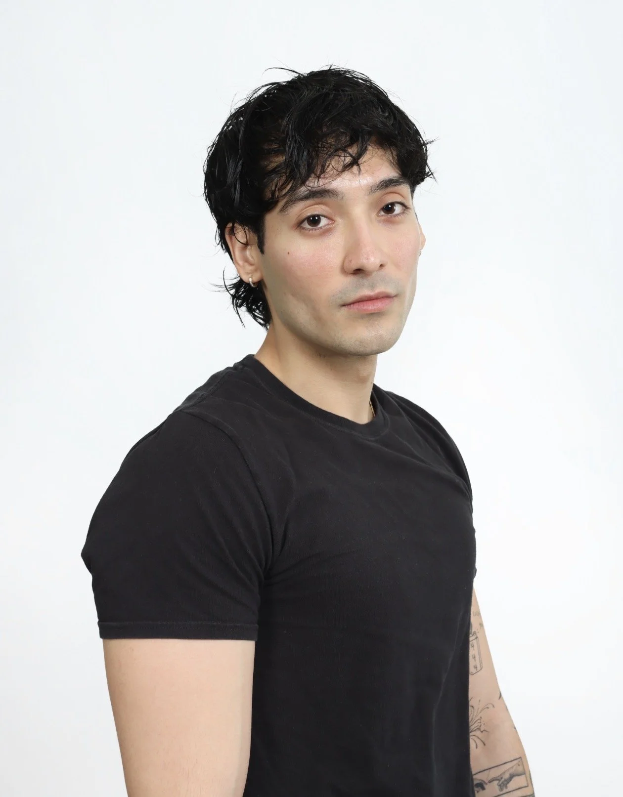 Jordan Campos with black wavy hair, wearing a black t-shirt, looking at the camera against a white background with direct gaze portrait and a strong on-camera expression.