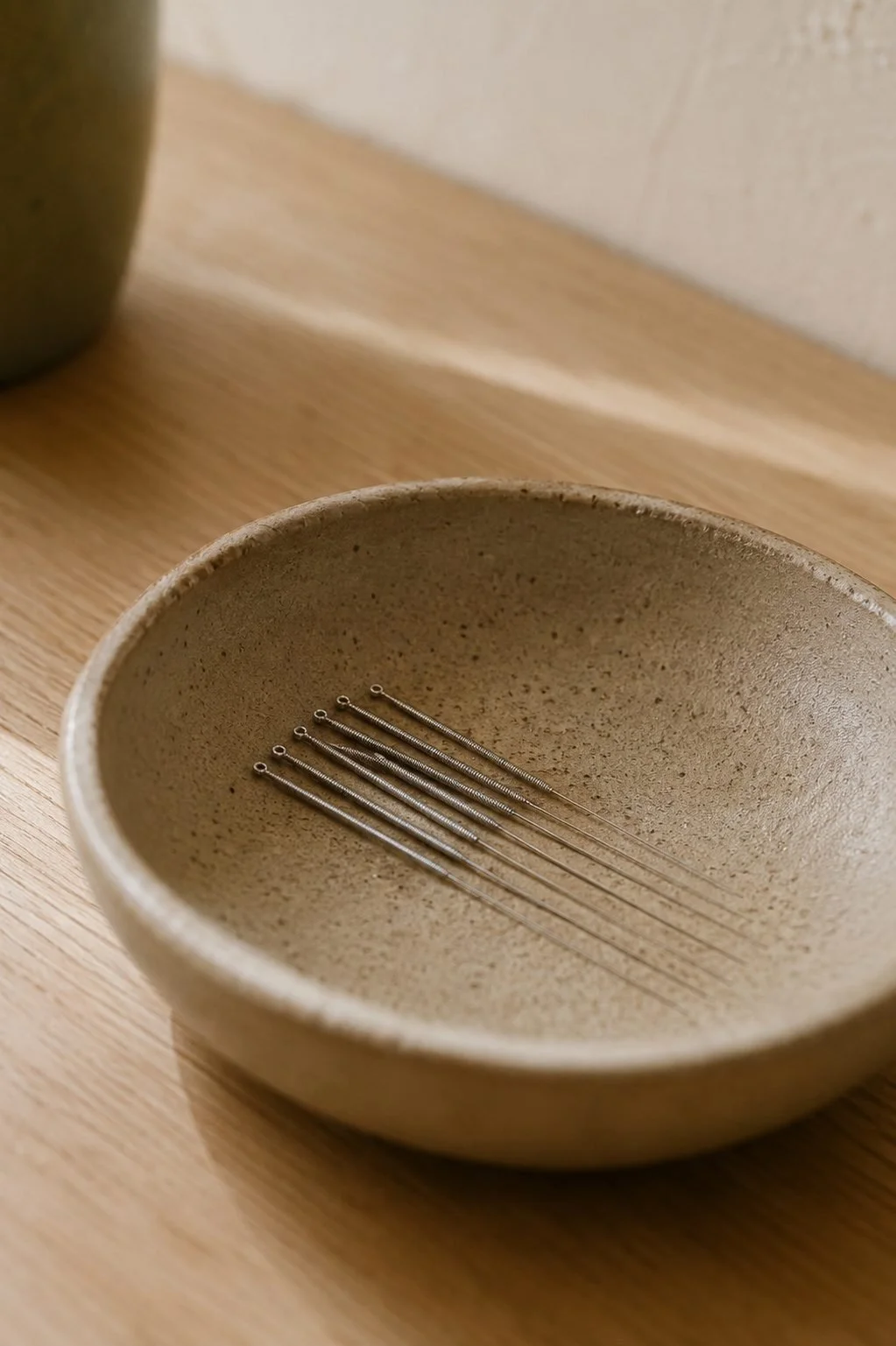 A beige ceramic bowl containing six metal acupuncture needles on a wooden surface.
