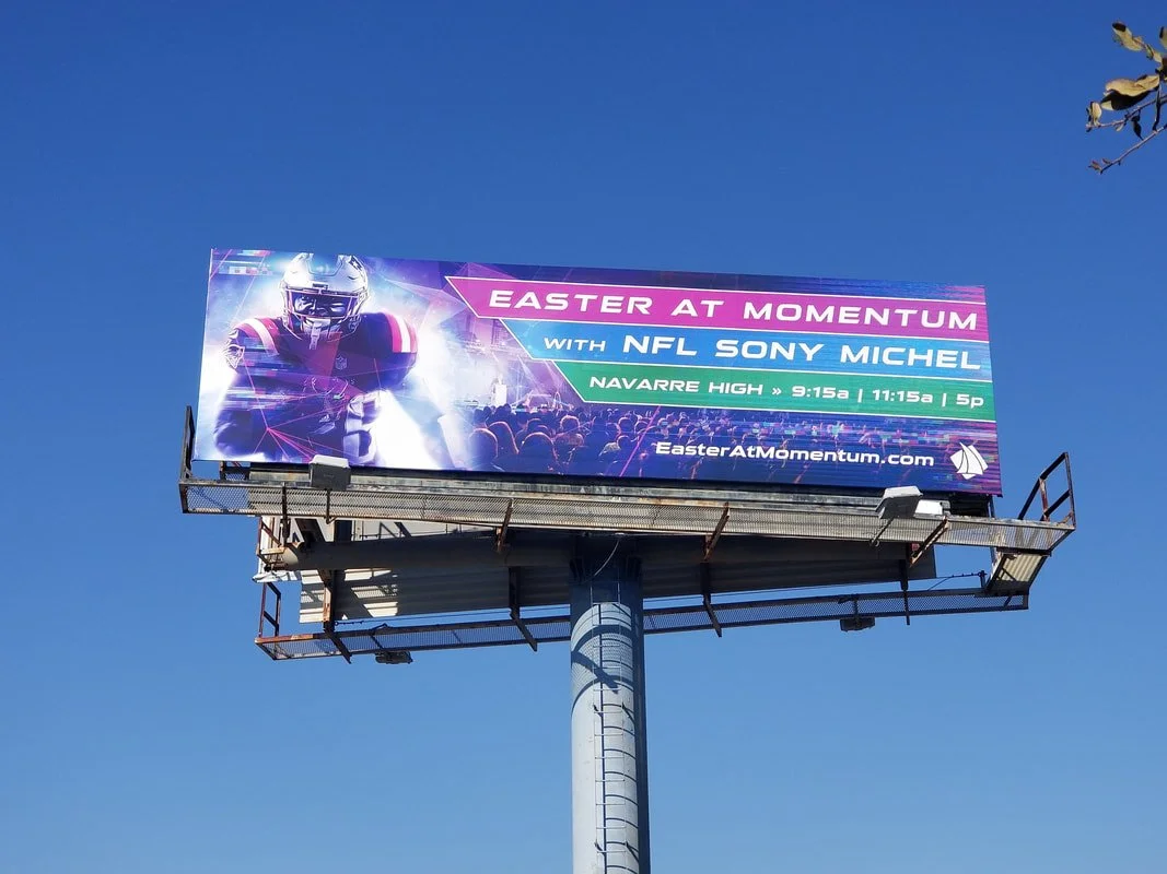 Billboard advertising an event called Easter at Momentum featuring NFL player Sony Michel, with event details for Navarre High at 9:15 am, 11:15 am, and 5 pm, and the website EasterAtMomentum.com.