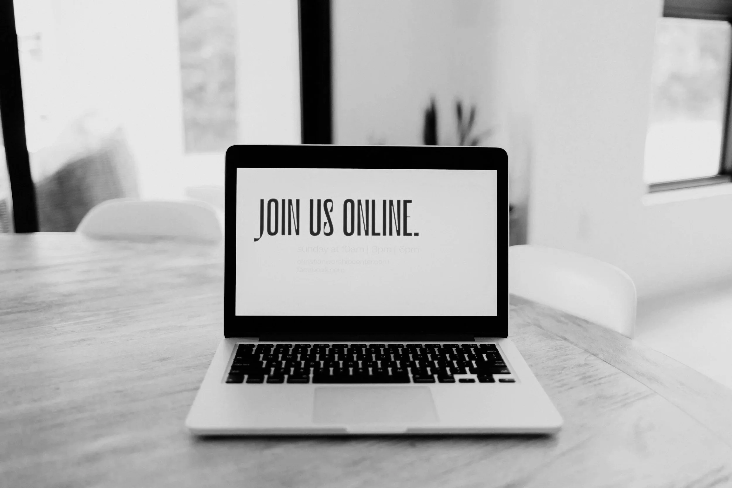 Black and white image of a laptop on a wooden table with a screen displaying 'Join us online' and event details.