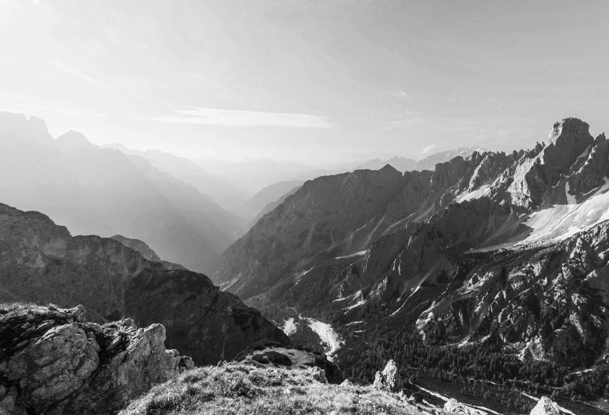 Black and white photograph of a mountain landscape with rugged peaks, steep slopes, and a valley with a winding river or road.
