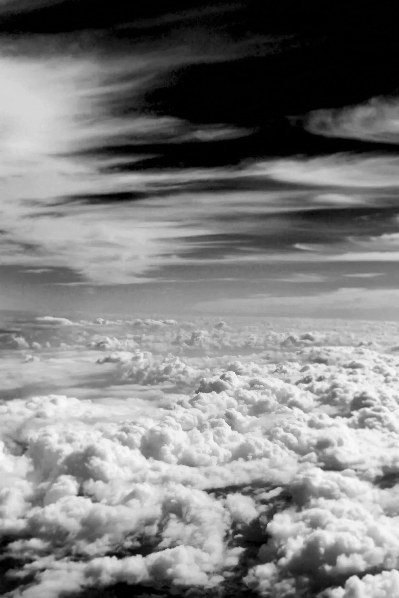 Black and white photo of clouds from above, with a dramatic sky featuring streaks of dark and light clouds.