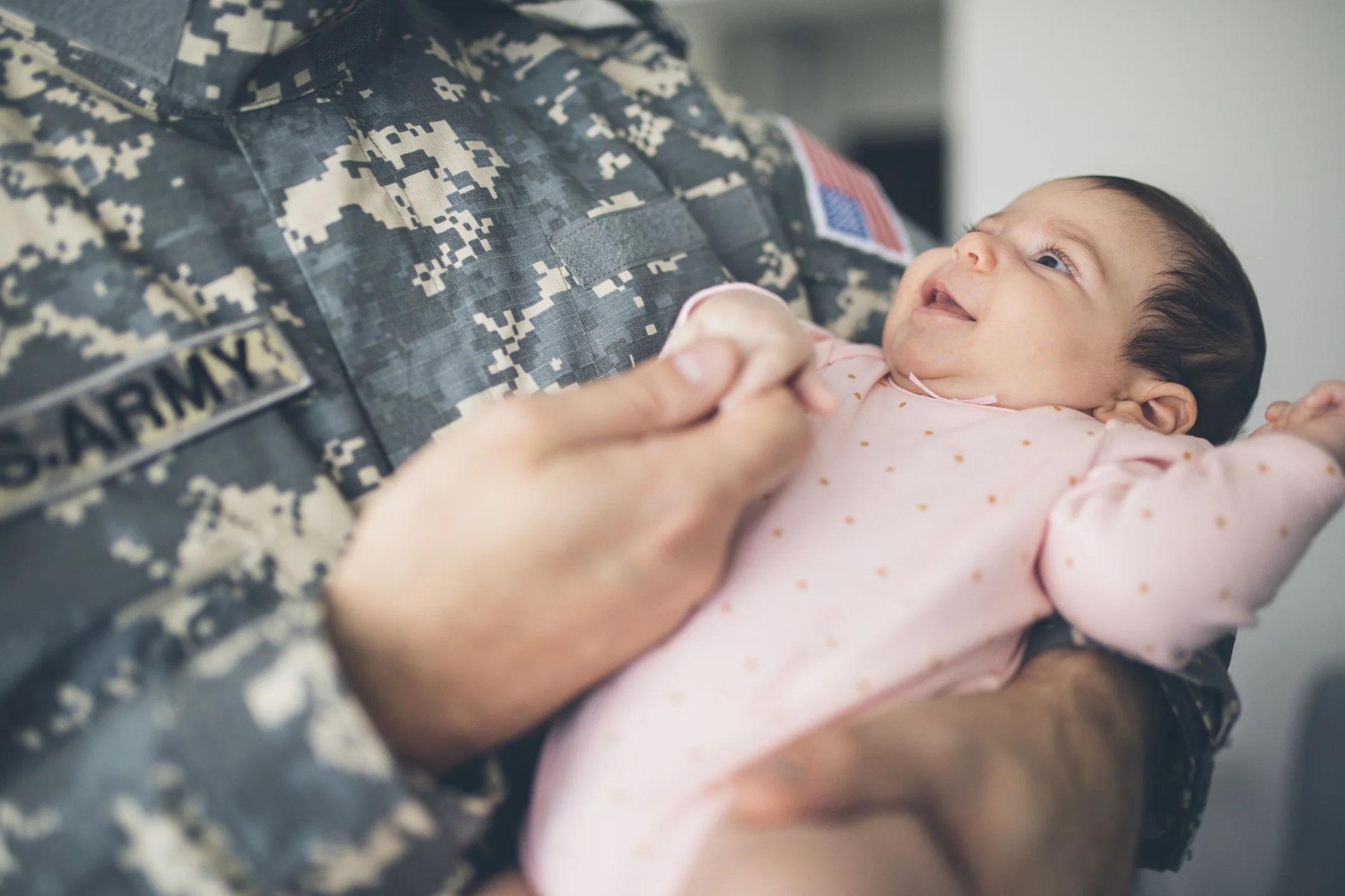 A soldier in uniform holding a baby and smilin.