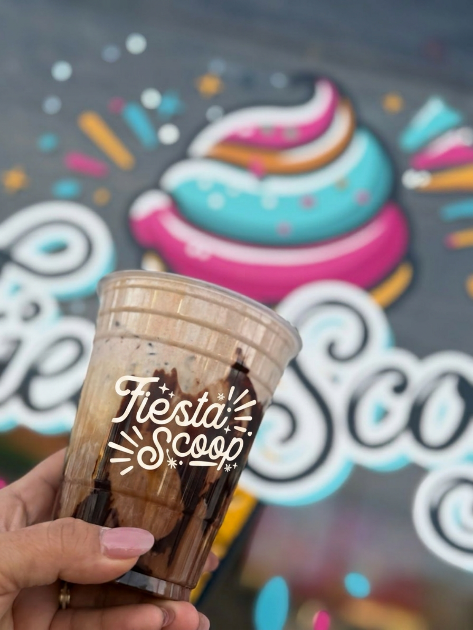 Person holding a plastic cup of ice cream with the words 'Fiesta Scoop' printed on it. The background contains colorful, festive, swirl and dot designs.