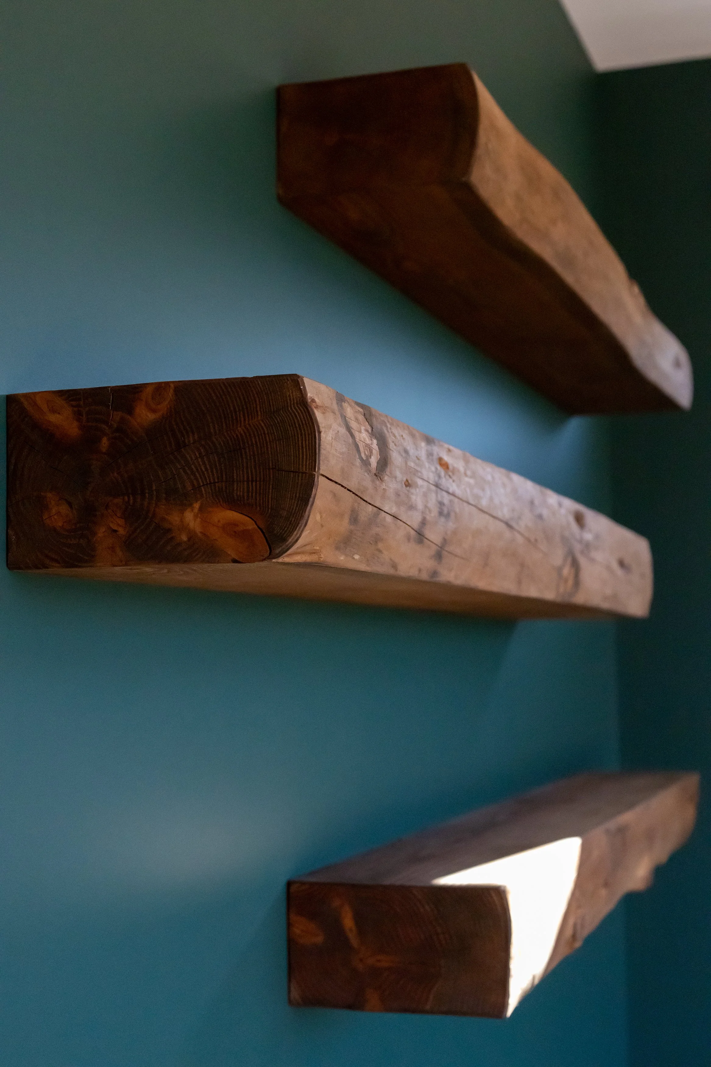 Three rustic wooden shelves mounted on a teal wall.