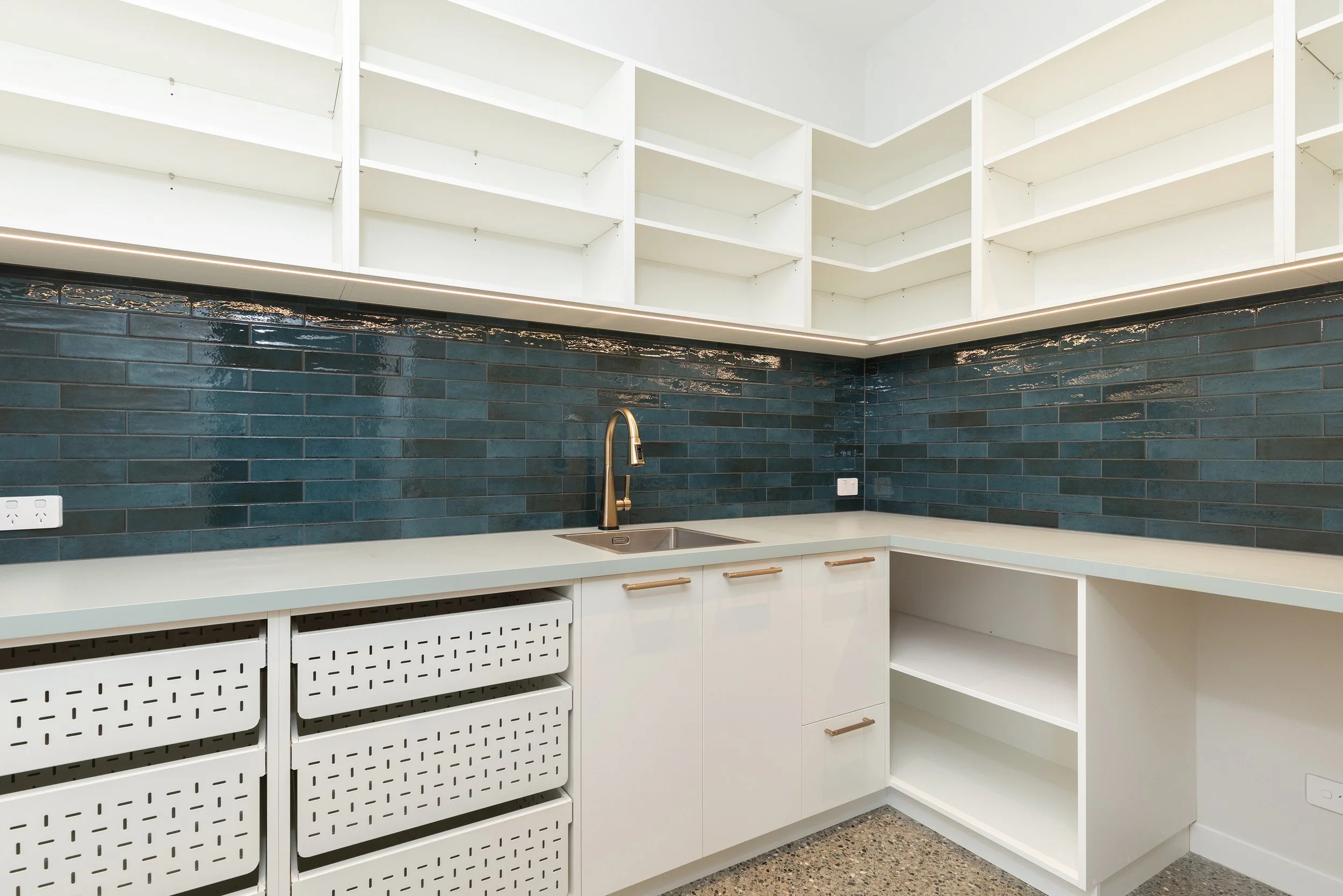 Empty kitchen with white cabinets, open shelves, a black tile backsplash, and a gold faucet over a small sink.