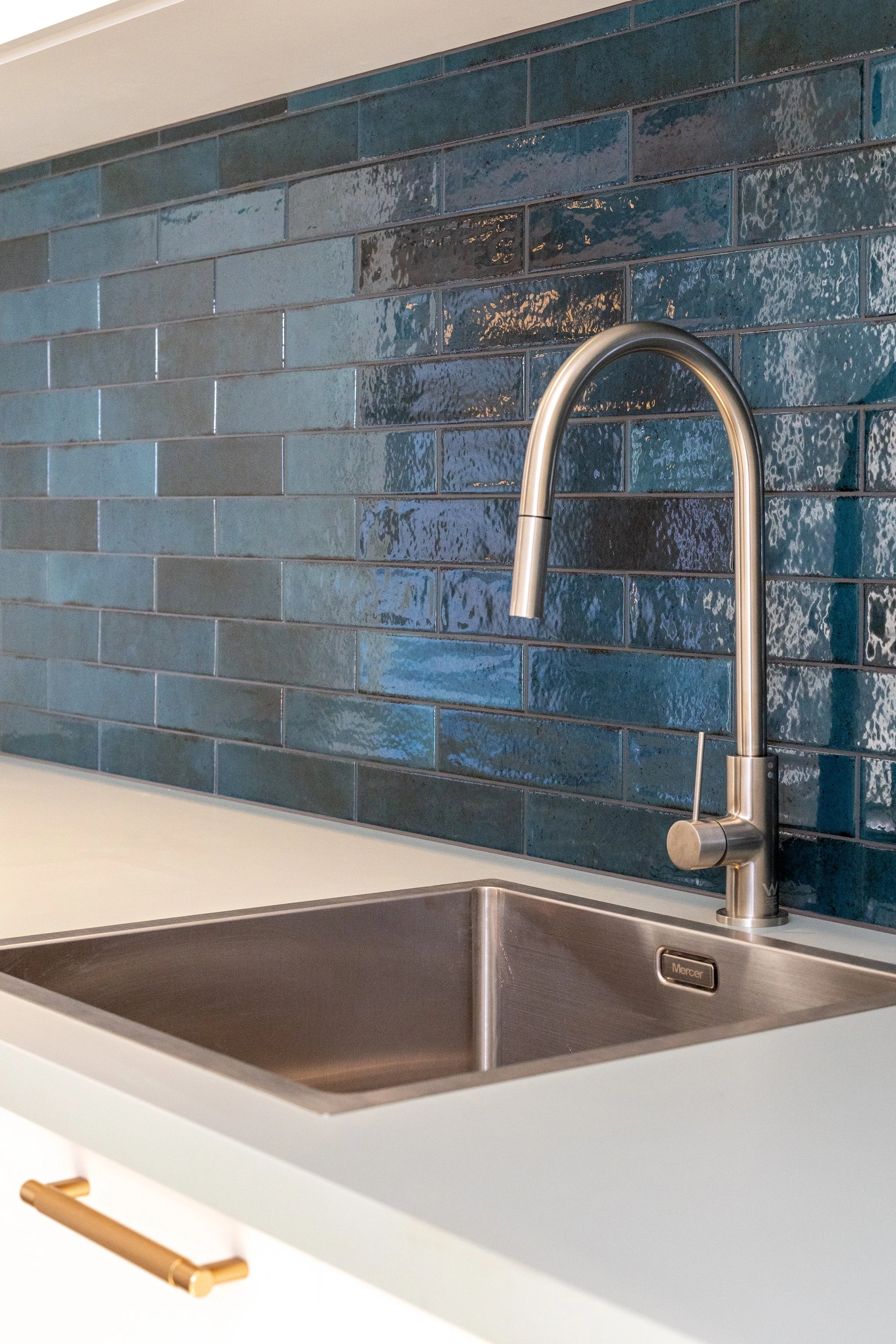 Kitchen with a stainless steel sink, modern faucet, white countertop, and a dark blue tiled backsplash.