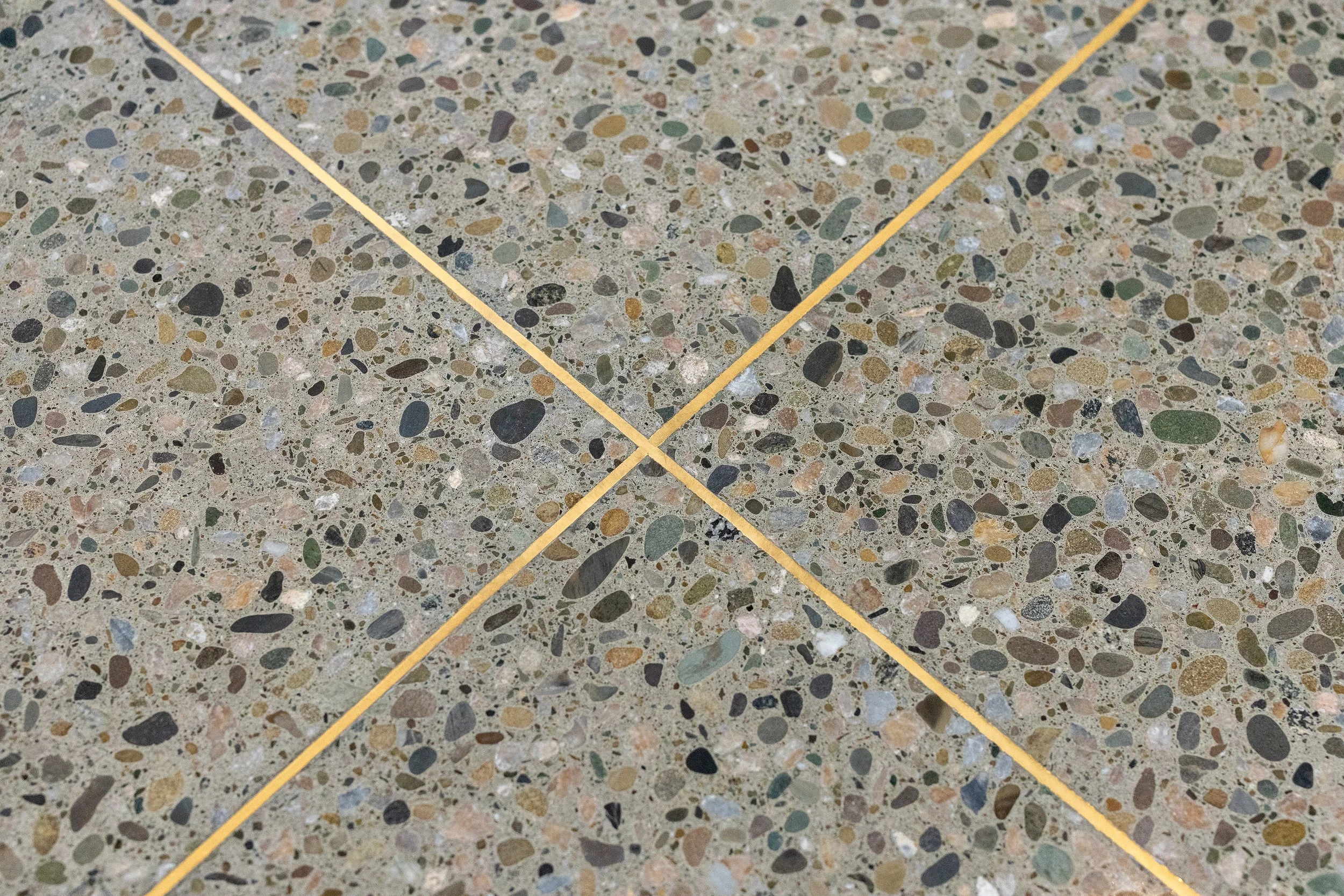 Close-up of a terrazzo floor with yellow grout lines forming a cross. The floor surface is speckled with small multi-colored stones.