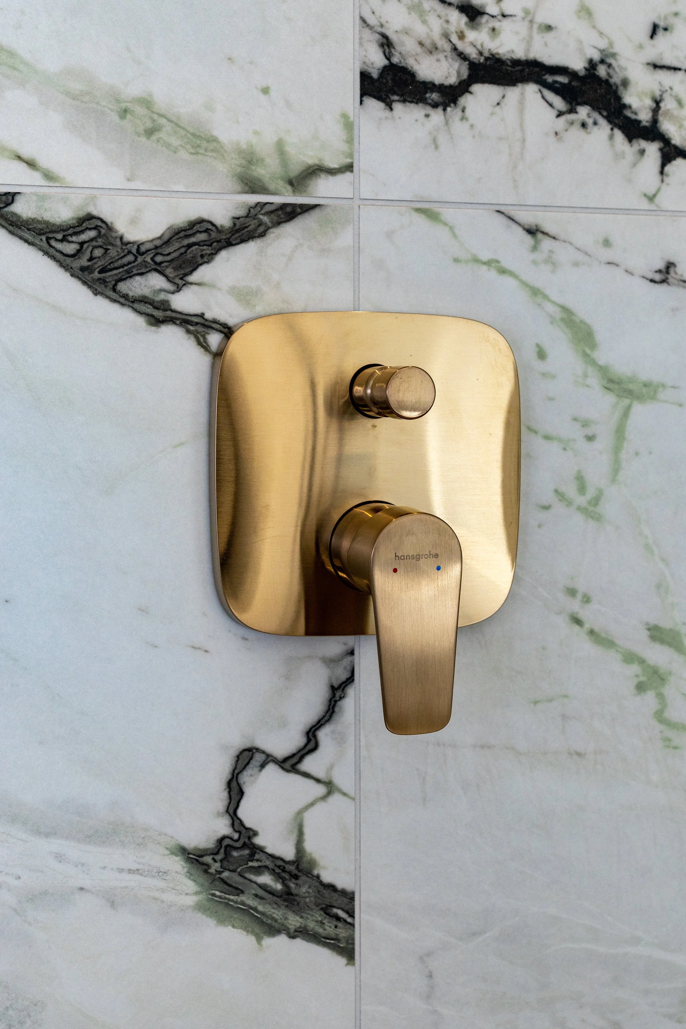 Close-up of a gold-colored shower wall control handle on marble tile wall.