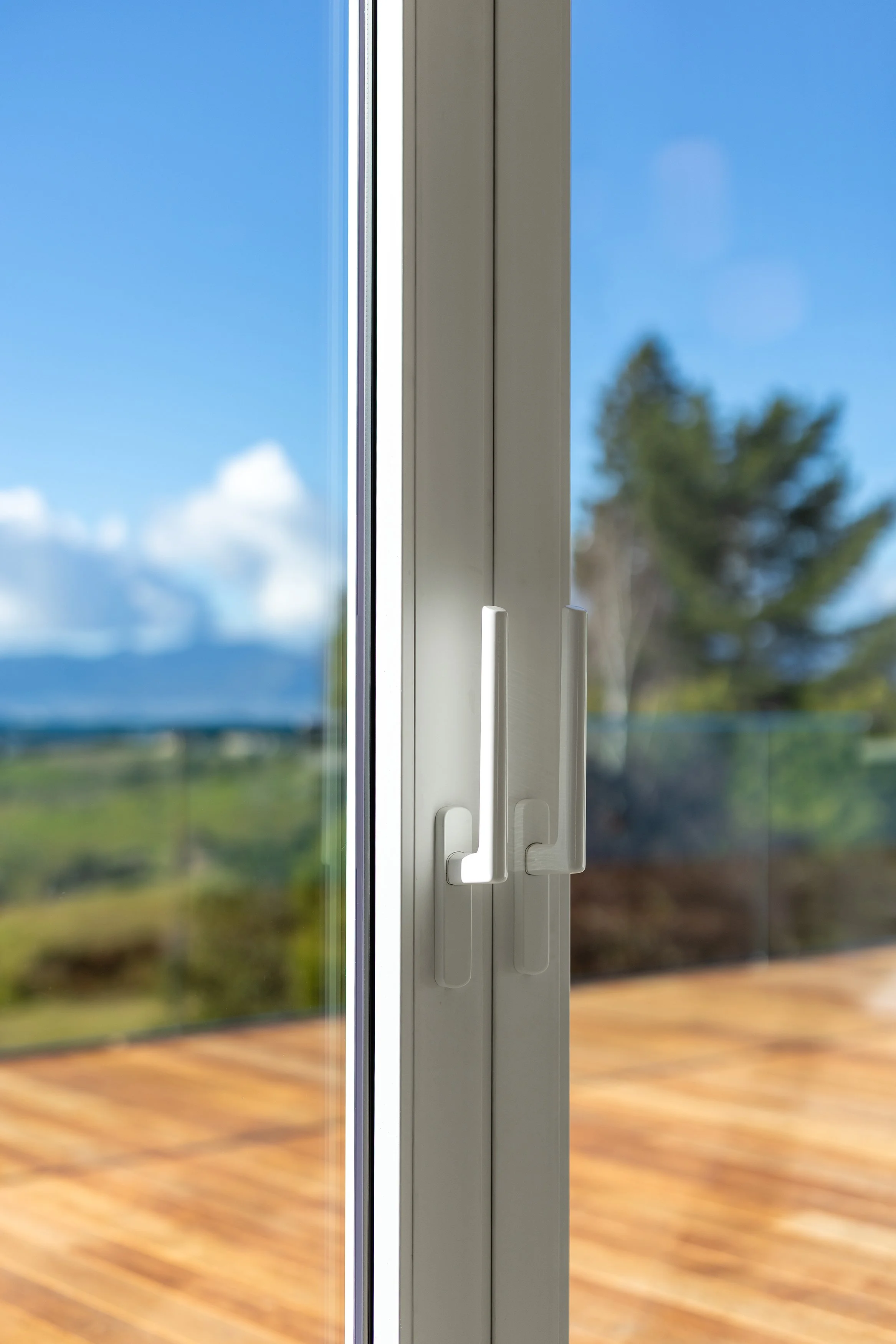 Close-up of a sliding glass door handle with a scenic outdoor view of a deck, trees, and a blue sky with clouds.