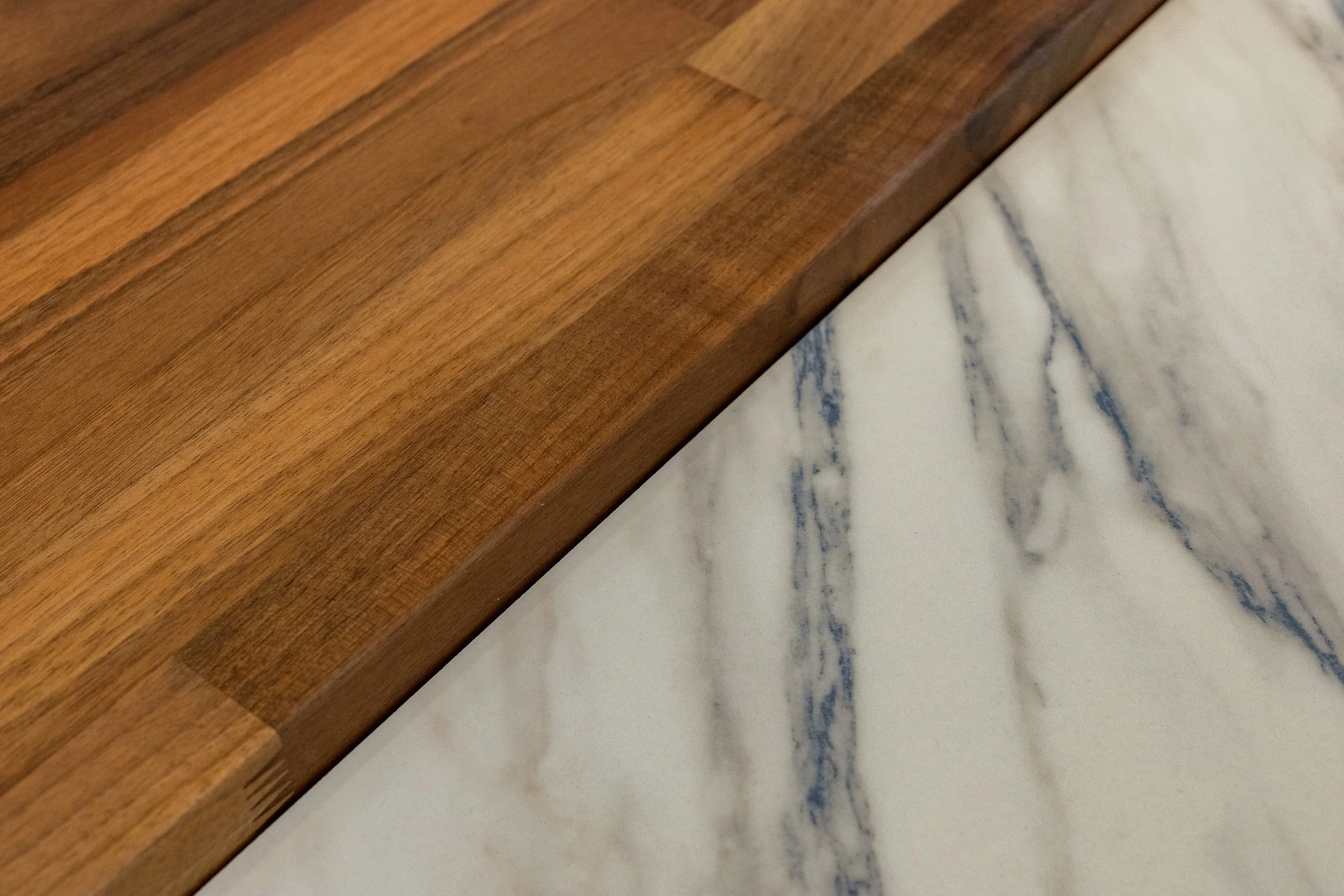 Close-up of a timber kitchen benchtop meeting a marble benchtop surface, showing a sharp edge and contrasting textures.
