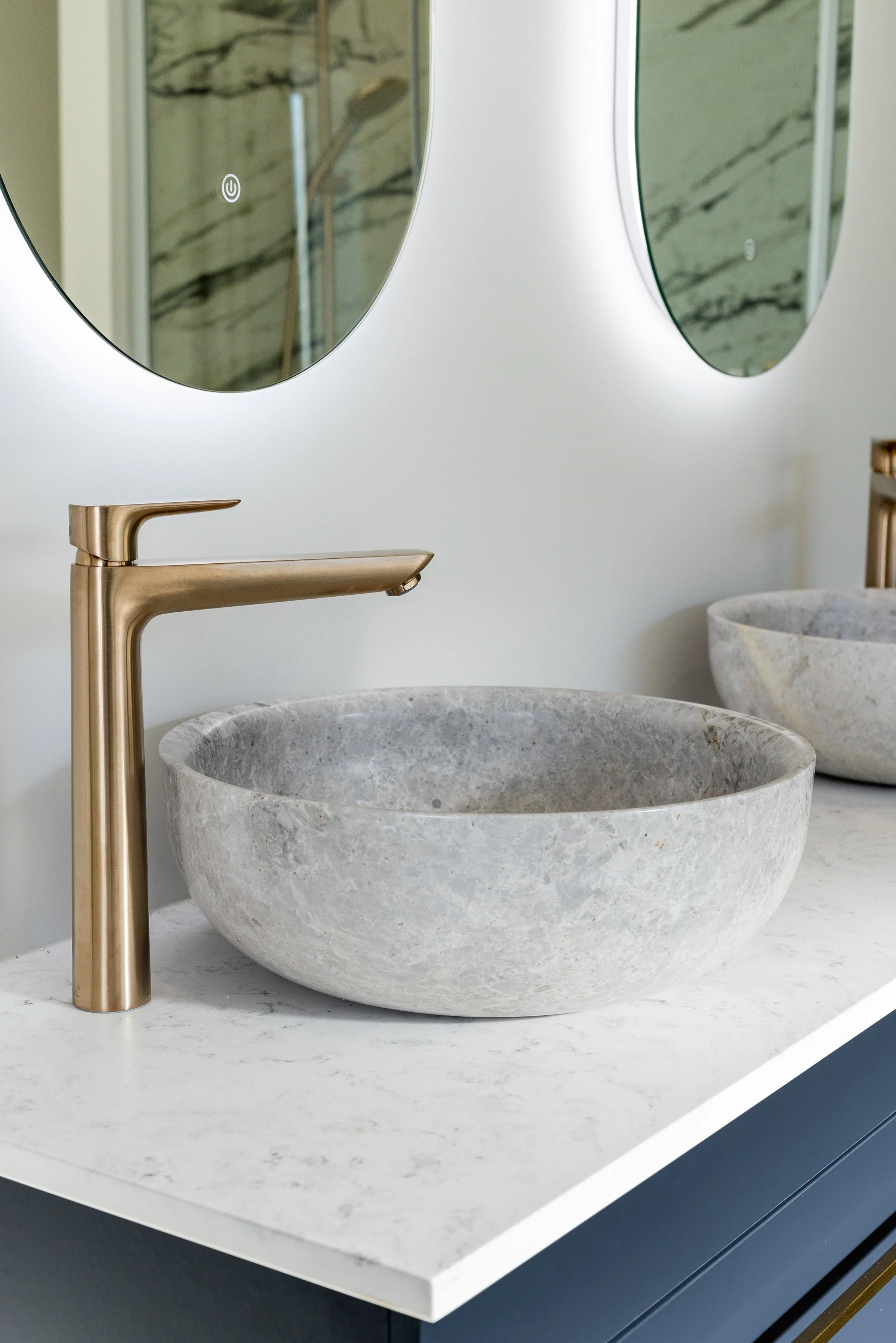 A bathroom sink with a brass faucet, a stone basin, a mirror, and a marble countertop.