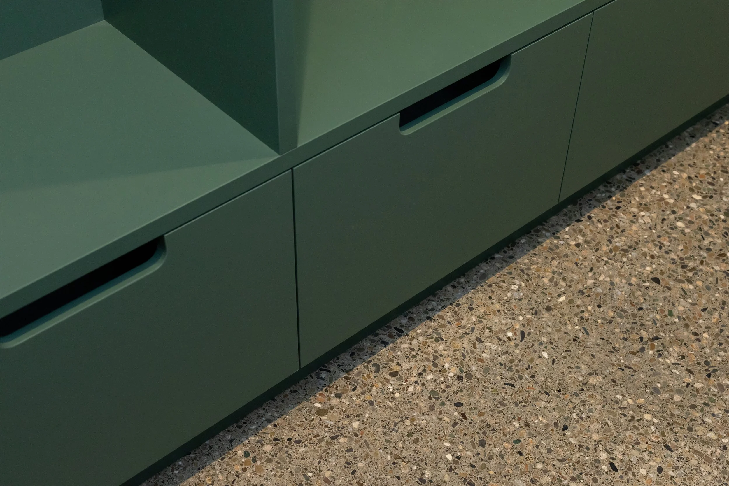 Close-up of green cabinetry with polished concrete flooring.