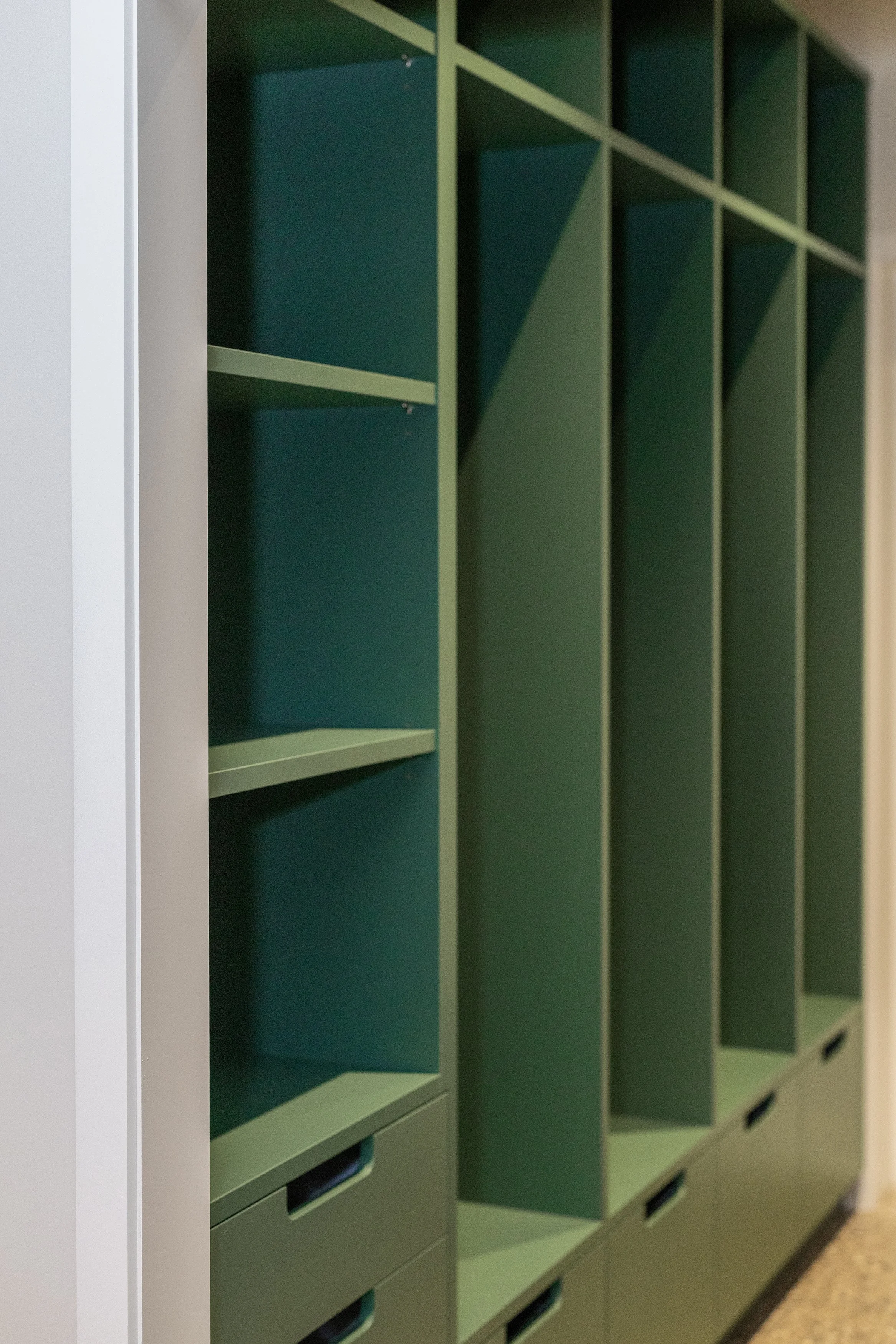 Green cubed storage lockers with open shelves and drawers, set against a beige wall.