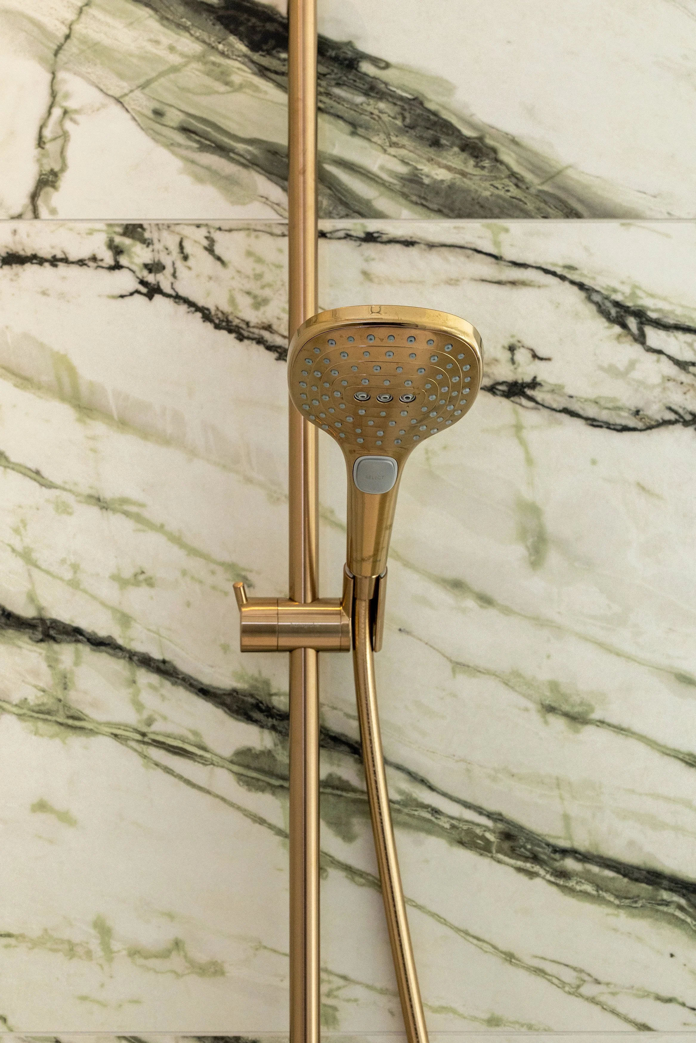 Close-up of a gold-colored showerhead mounted on a marble wall in a bathroom.