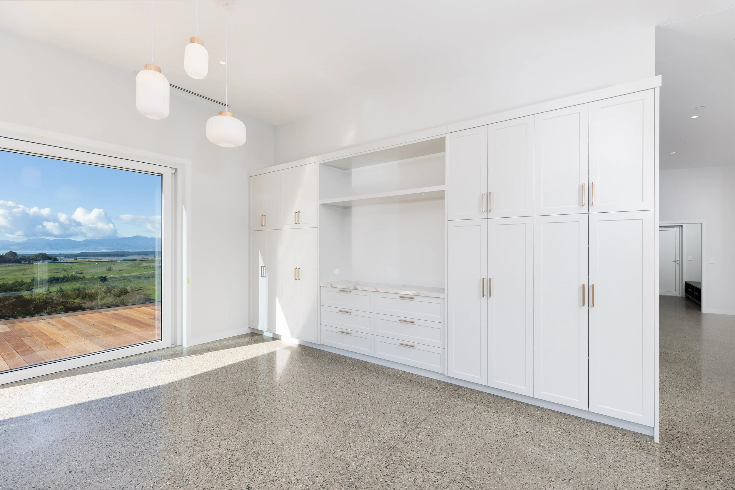 Modern kitchen with white cabinets, granite countertops, and large sliding glass door overlooking a scenic landscape with mountains and blue sky.