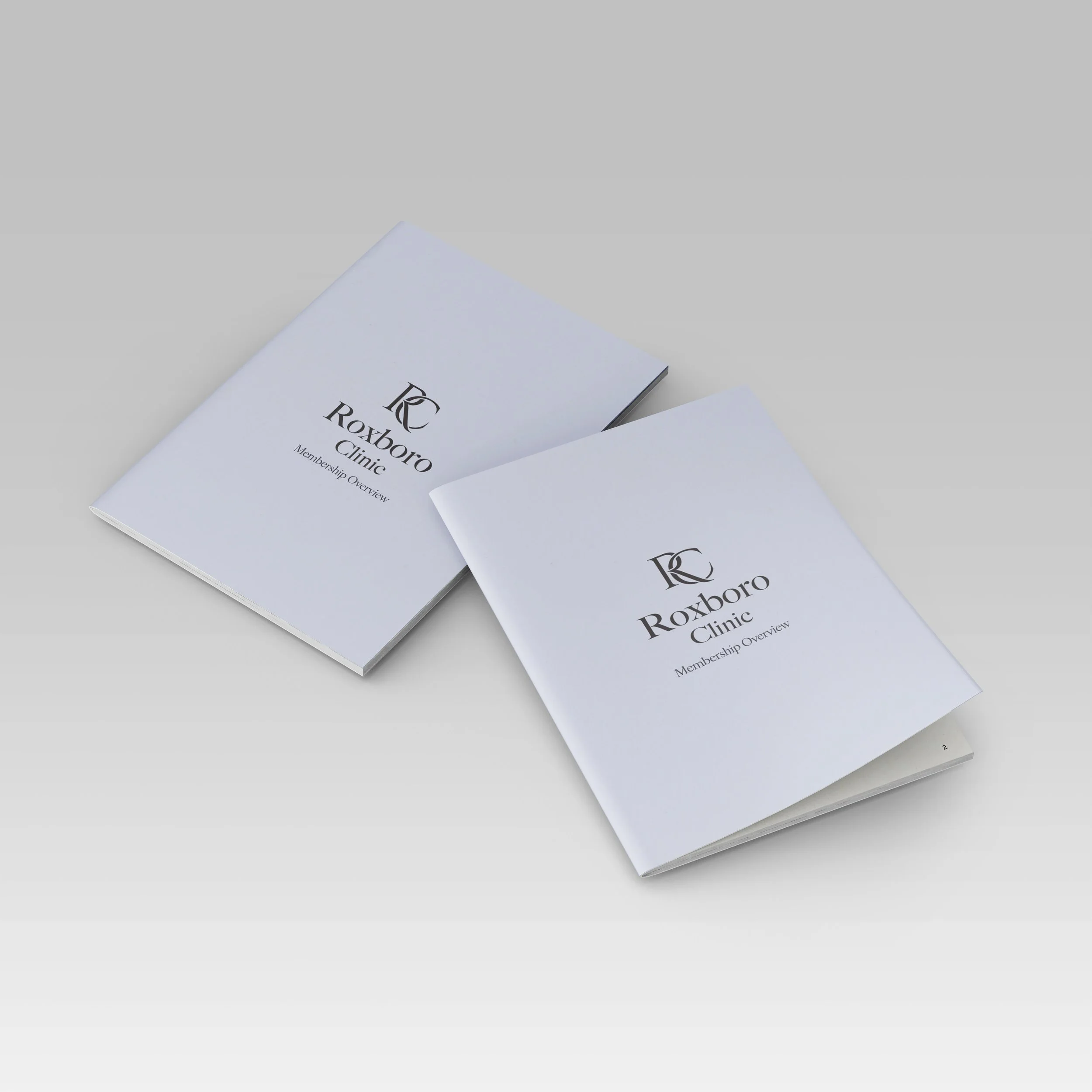Two white booklets titled 'Roxboro Clinic Membership Overview' with black text and logo, placed on a light gray background.