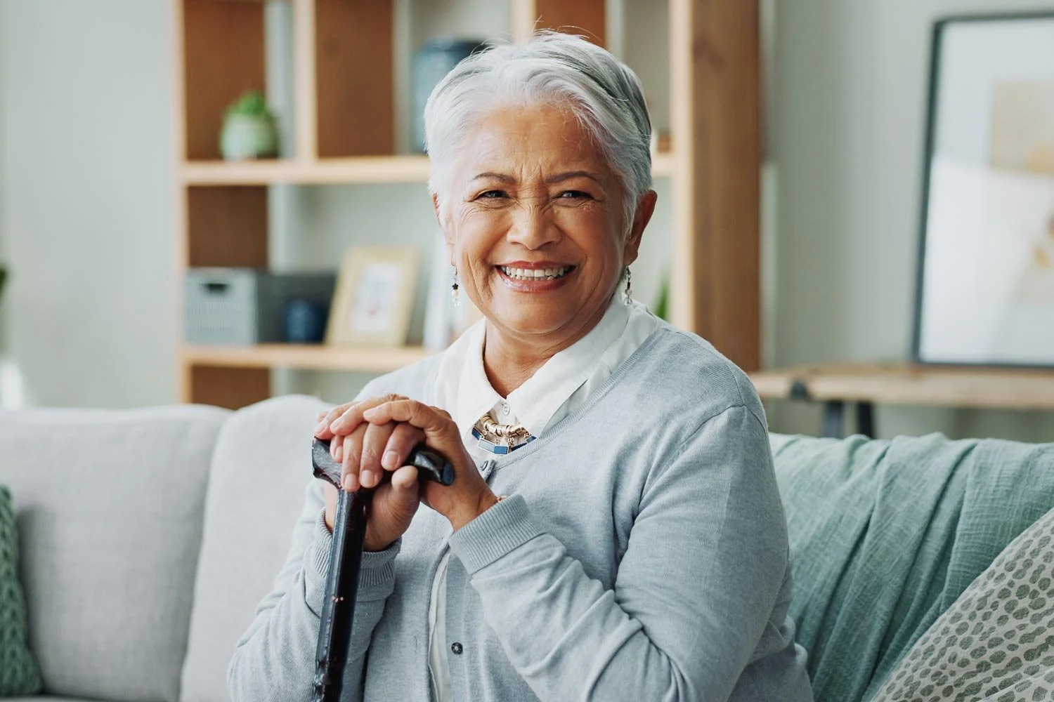 Senior woman smiling with hands resting on cane handle.
