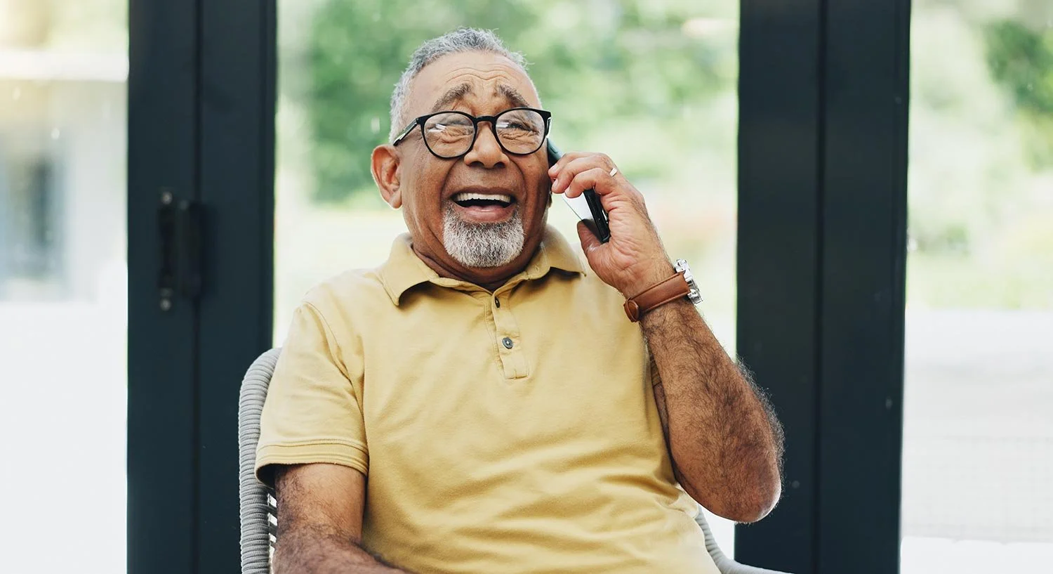 Smiling older man in yellow shirt talks on a smartphone.