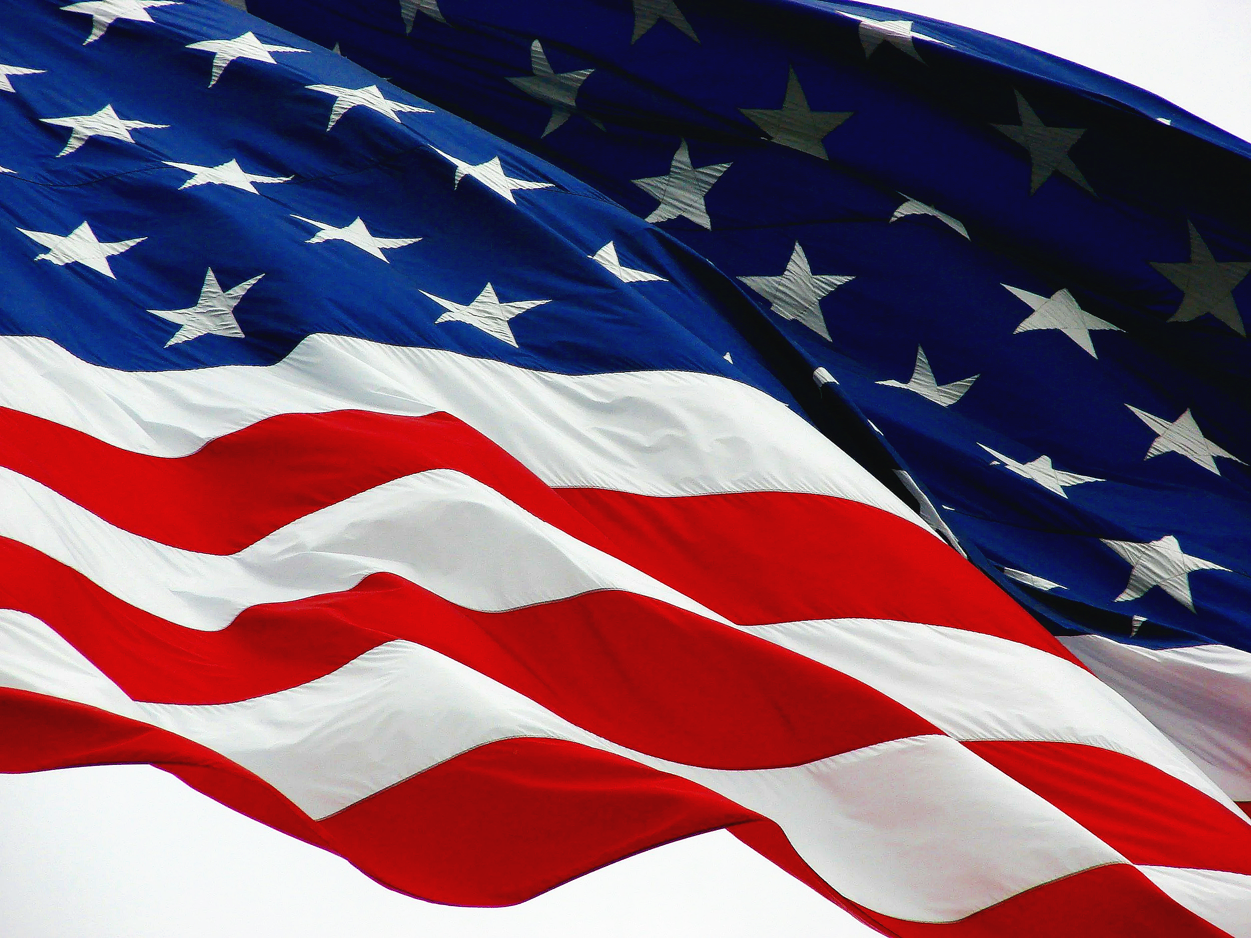 American flags waving in the wind with red, white, and blue colors and white stars on a blue field.