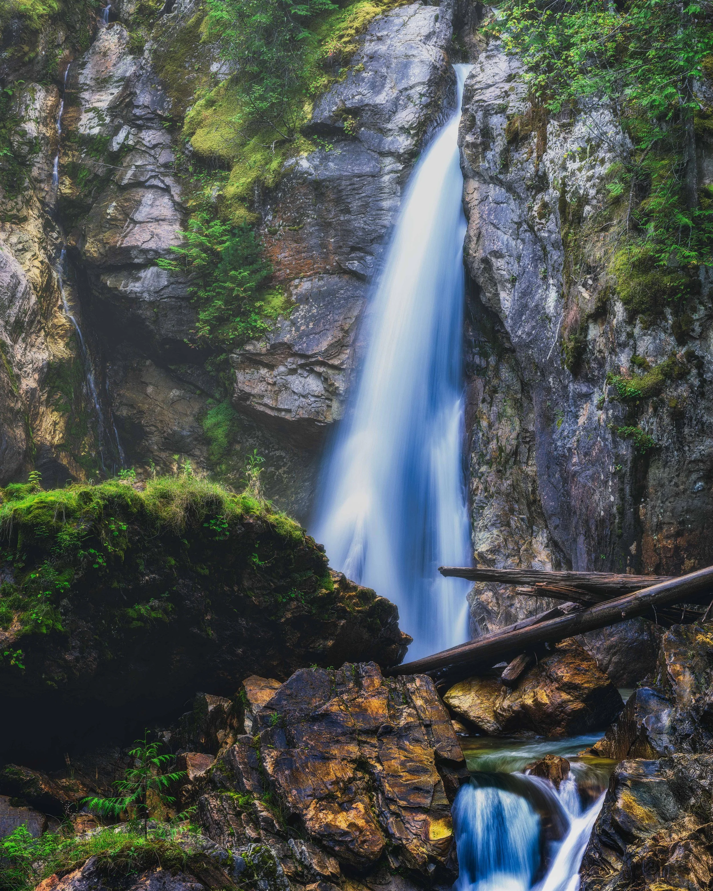 A tall waterfall flowing down a rocky cliffside surrounded by lush green foliage.