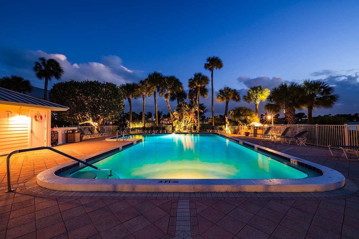 Illuminated outdoor swimming pool at dusk with palm trees and lounge chairs
