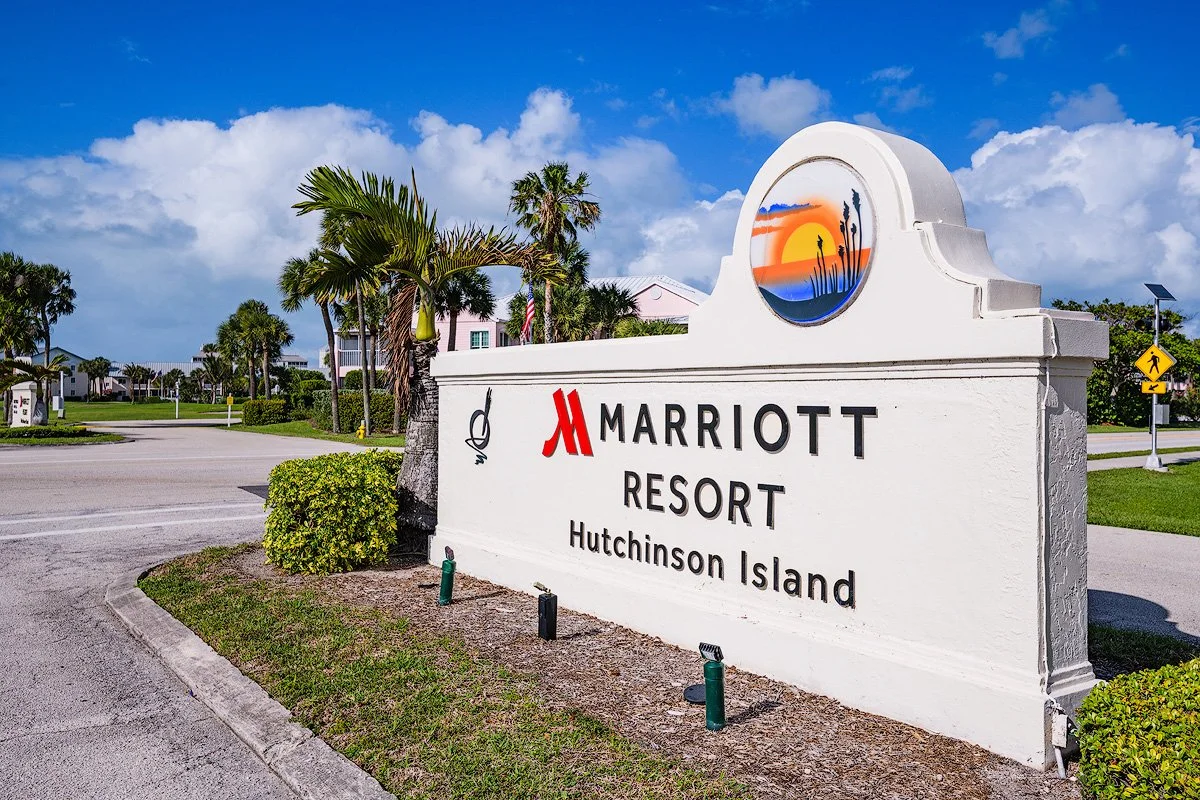 Entrance sign for Marriott Resort on Hutchinson Island, with palm trees, a clear blue sky, and a sunset logo on the sign.