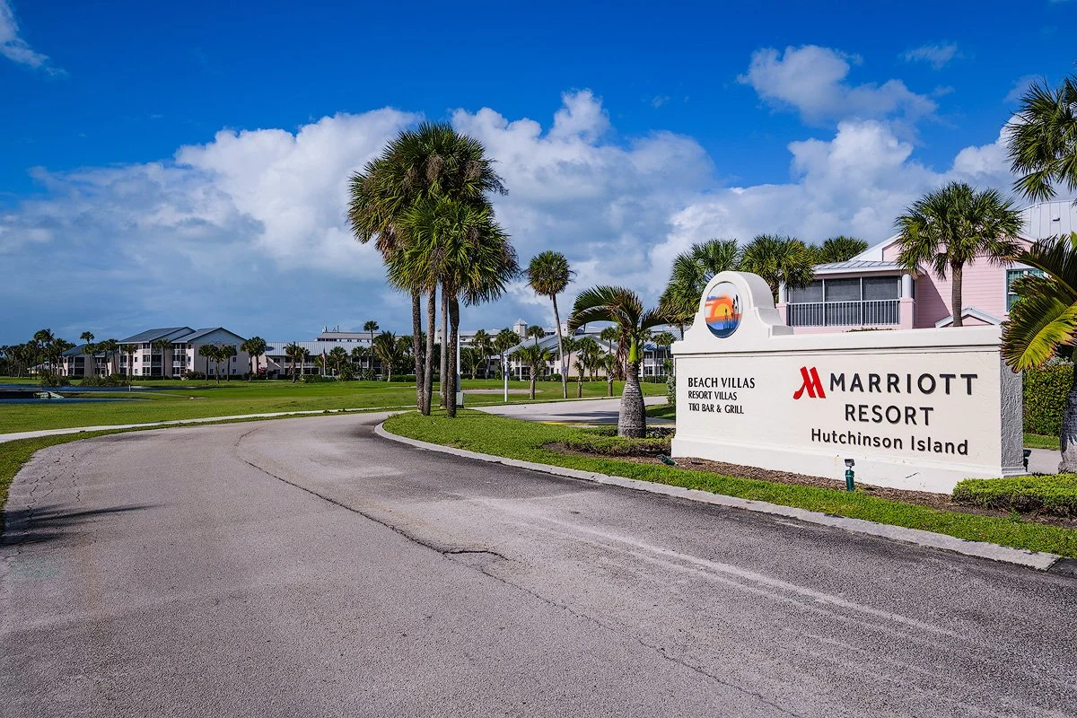 Entrance sign for Marriott Resort on Hutchinson Island with palm trees and resort buildings in the background, under a partly cloudy sky.