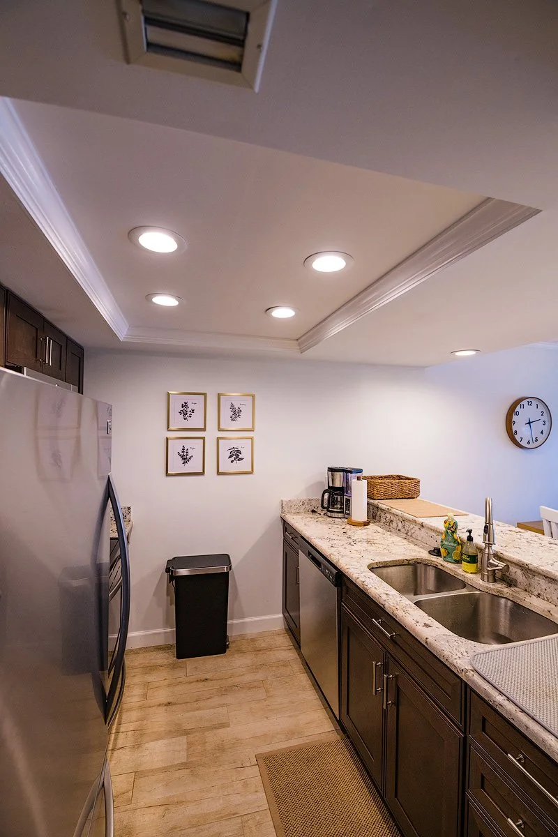 Kitchen with a granite countertop, double sink, coffee maker, wall clock, and framed botanical prints on the wall.