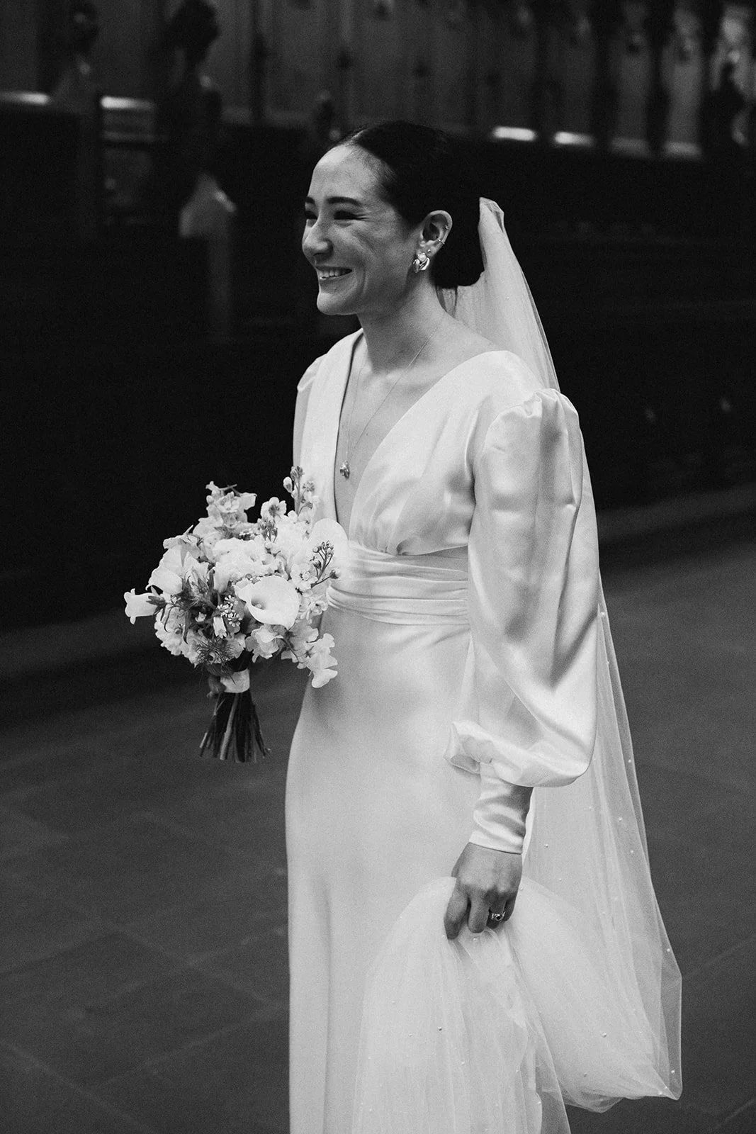 Smiling bride in wedding dress holding a bouquet of flowers.