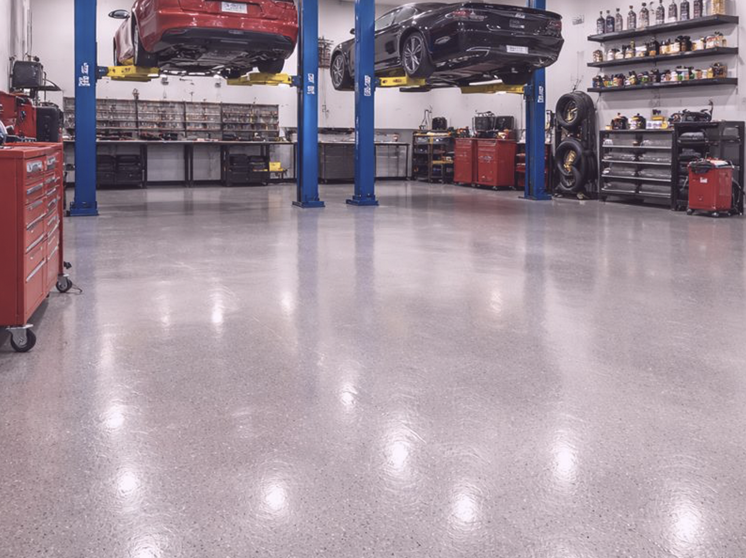 An automotive repair shop with two cars on hydraulic lifts and full chip system epoxy floor