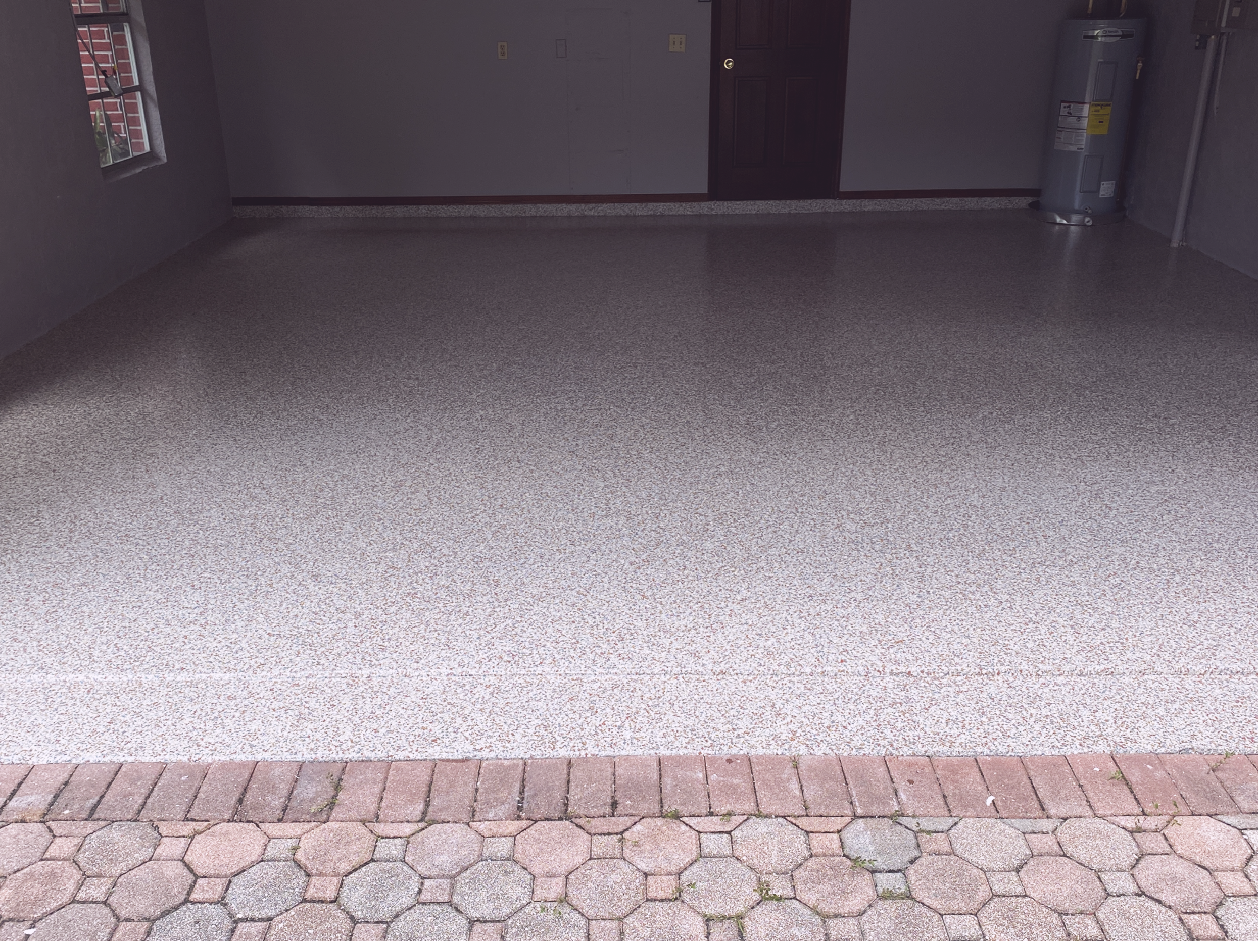 Empty garage with a brick pathway outside, remodeled epoxy flooring