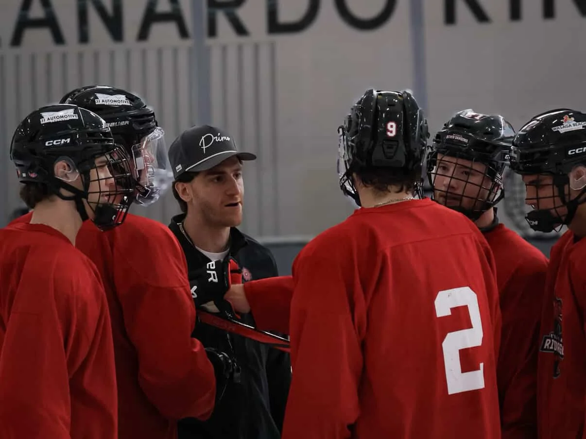Hockey players in red jerseys and helmets listening to coach during timeout.
