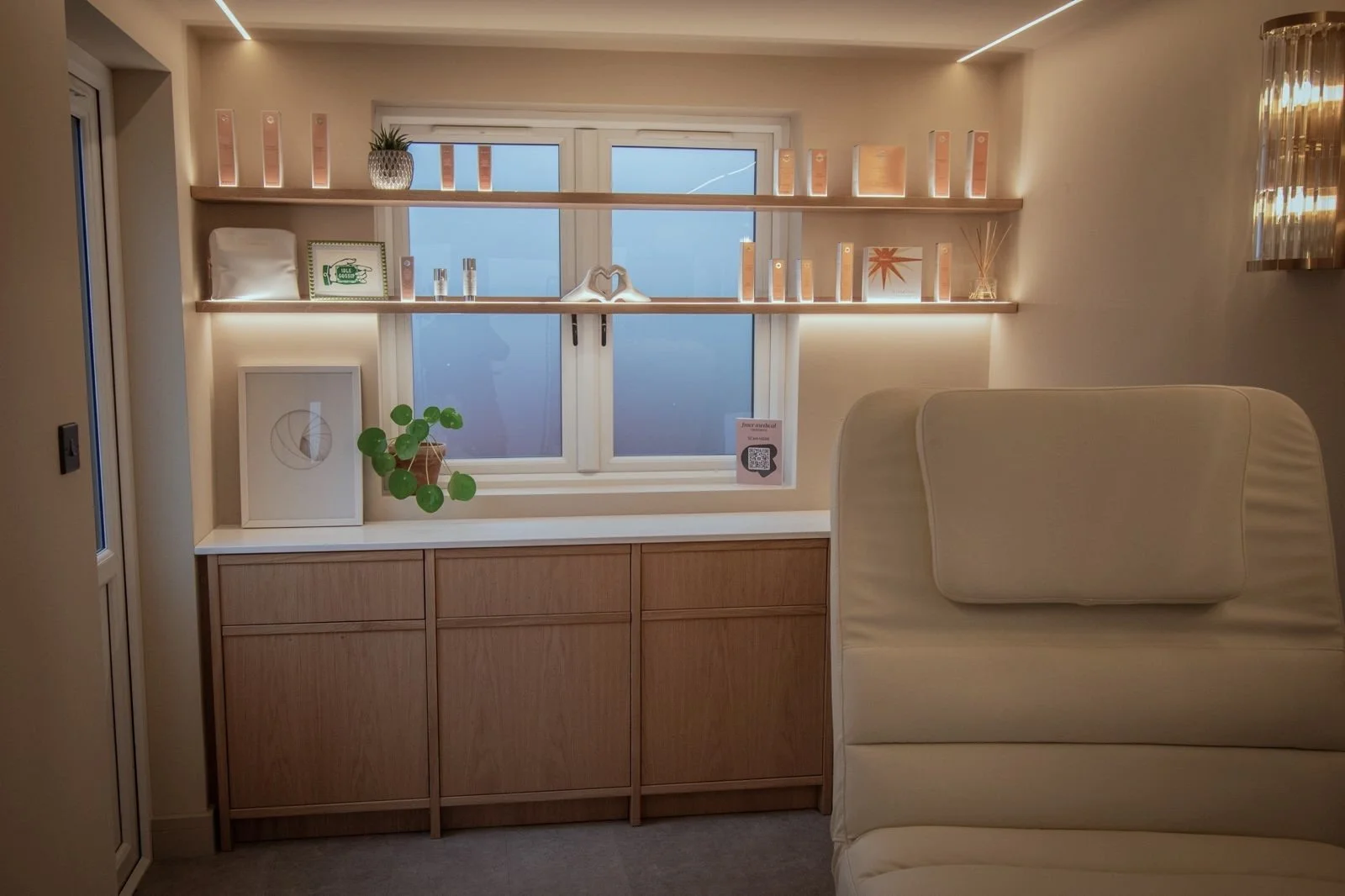 Finer Medical Aesthetics studio with large window, two wooden shelves with decor, framed art, a plant, and a white couch.