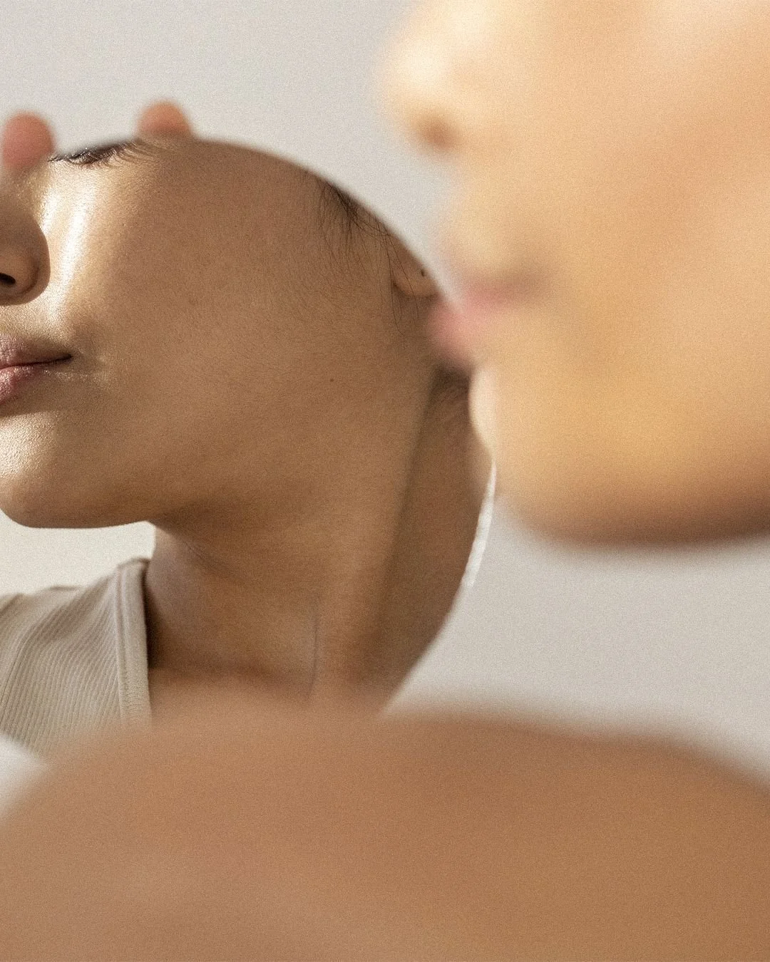 Close-up of a person's face with emphasis on their cheek and jawline, held in front of a mirror, showing their reflection.