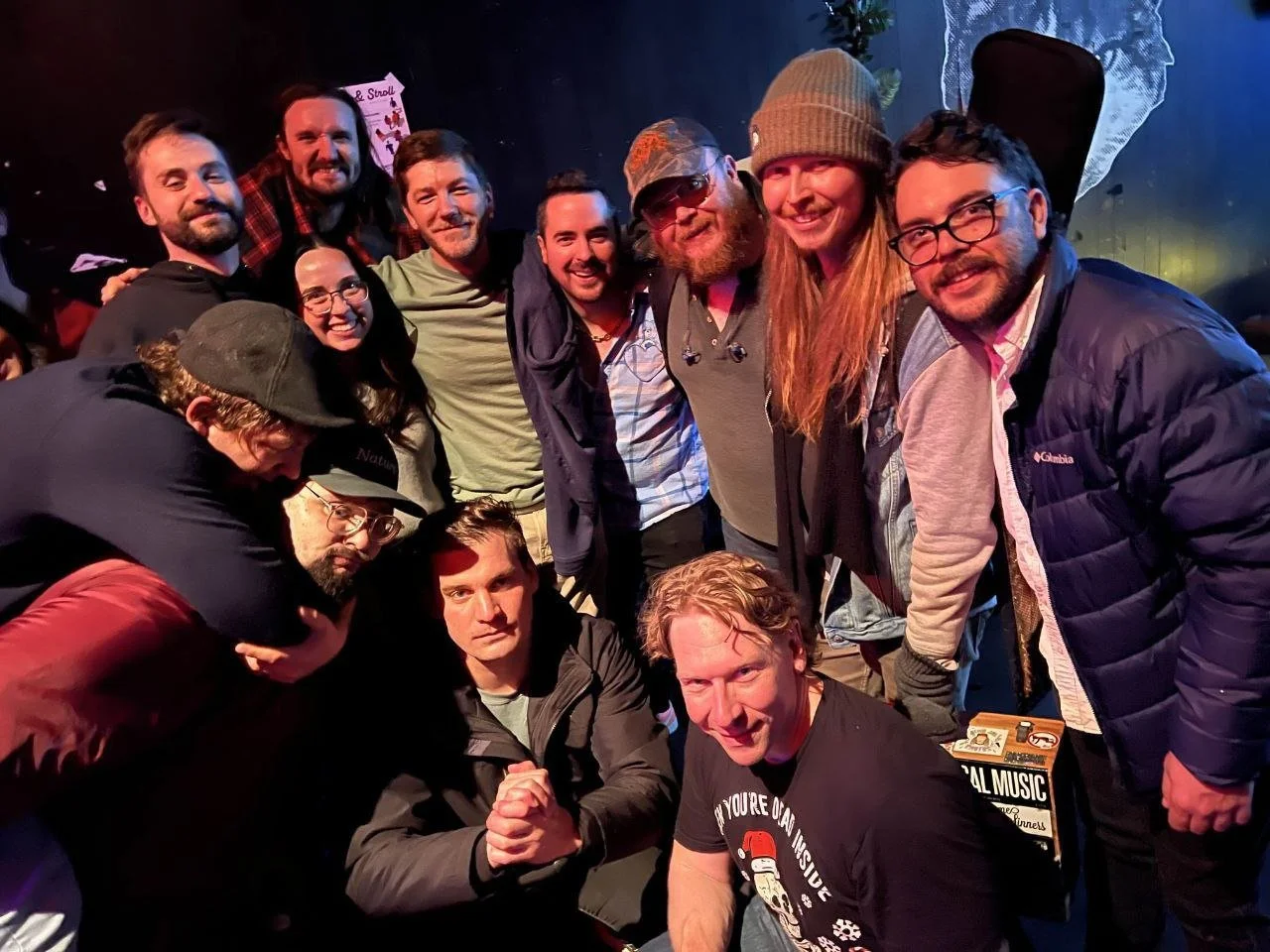 Group of people posing together at a social event, smiling and standing close under dim lighting.