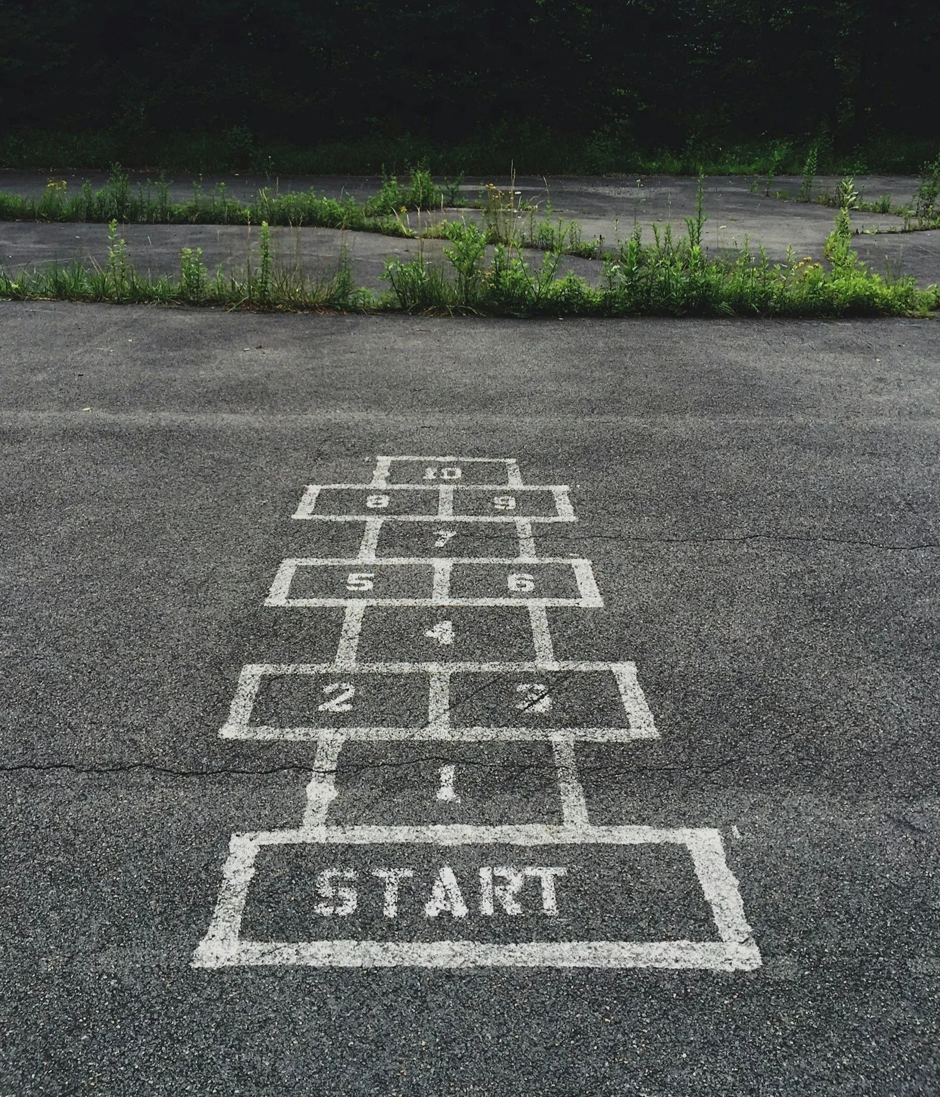 A hopscotch game drawn with white chalk on asphalt, starting with the word 'START' at the bottom and numbered squares from 1 to 10.