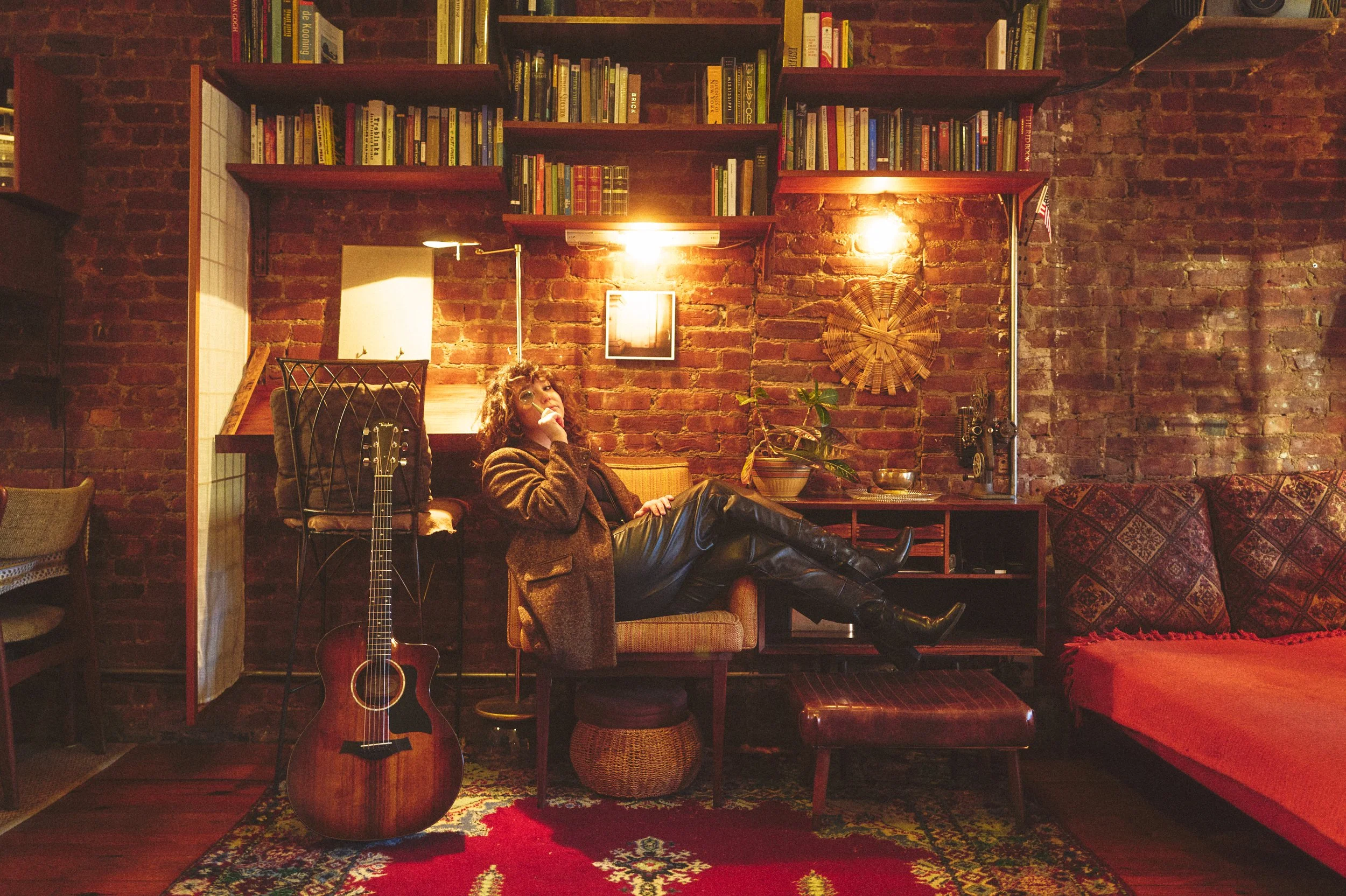 Portrait of Ellie Fern seated in a warm, book-lined studio with acoustic guitar