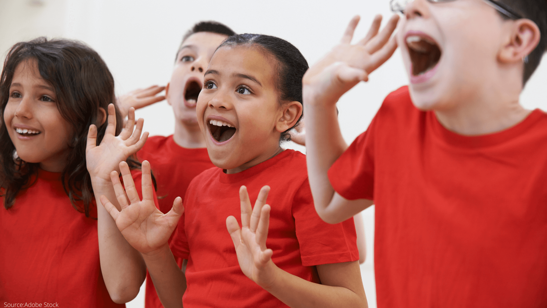 Group of children wearing red shirts, pretending to shout or call out, with cheerful expressions, indoors.