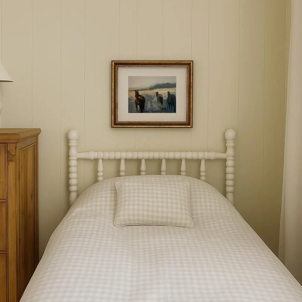 A neatly made bed with a light-colored checkered pillow, a white headboard, and a framed painting of horses hanging above it in a cozy room with beige paneled walls and a wooden wardrobe on the left.