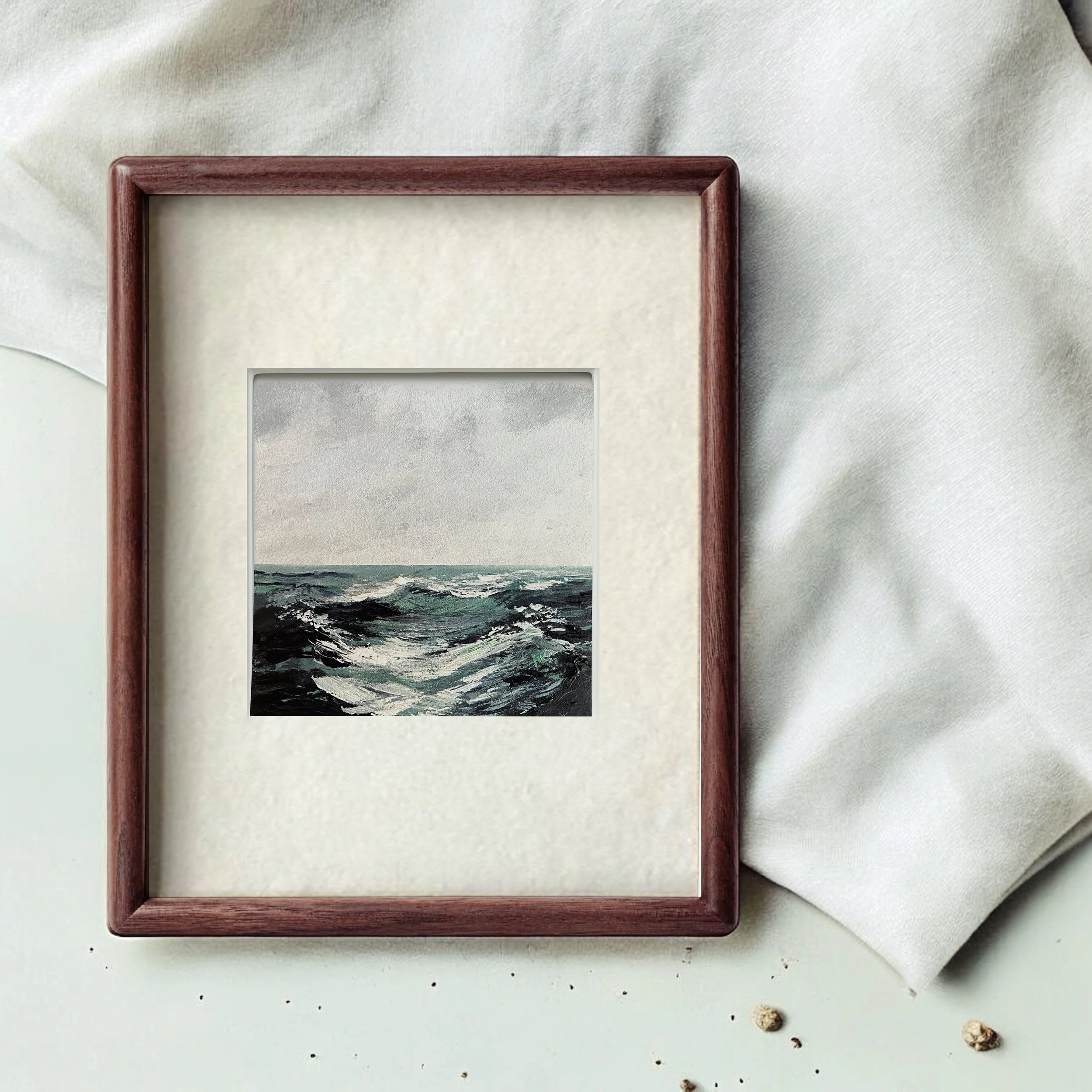 Framed acrylic painting of a stormy ocean with choppy waves, placed on a white surface with a light-colored fabric in the background.