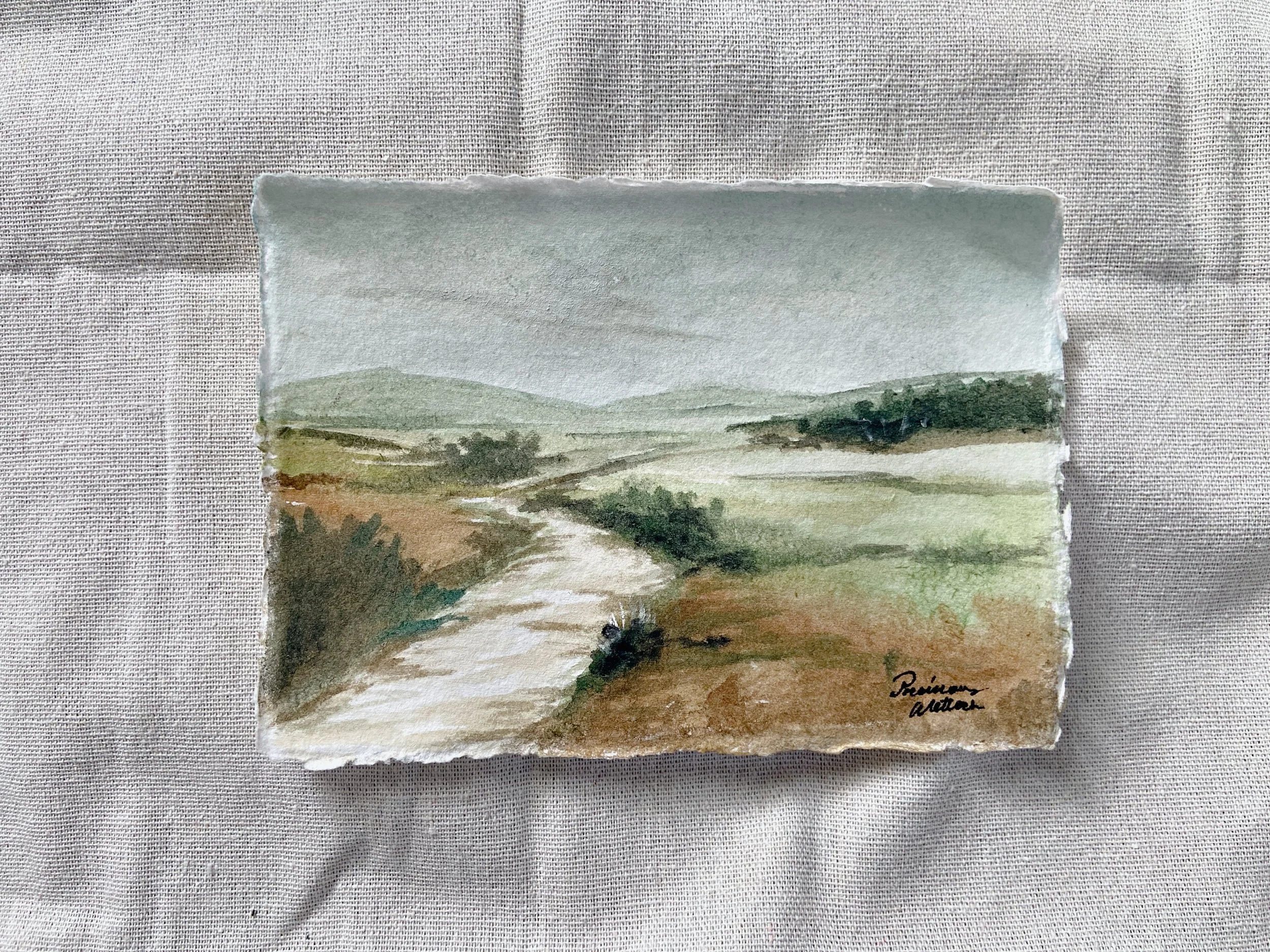 Watercolor painting of a countryside landscape with a winding dirt road, rolling hills, and trees under a cloudy sky.