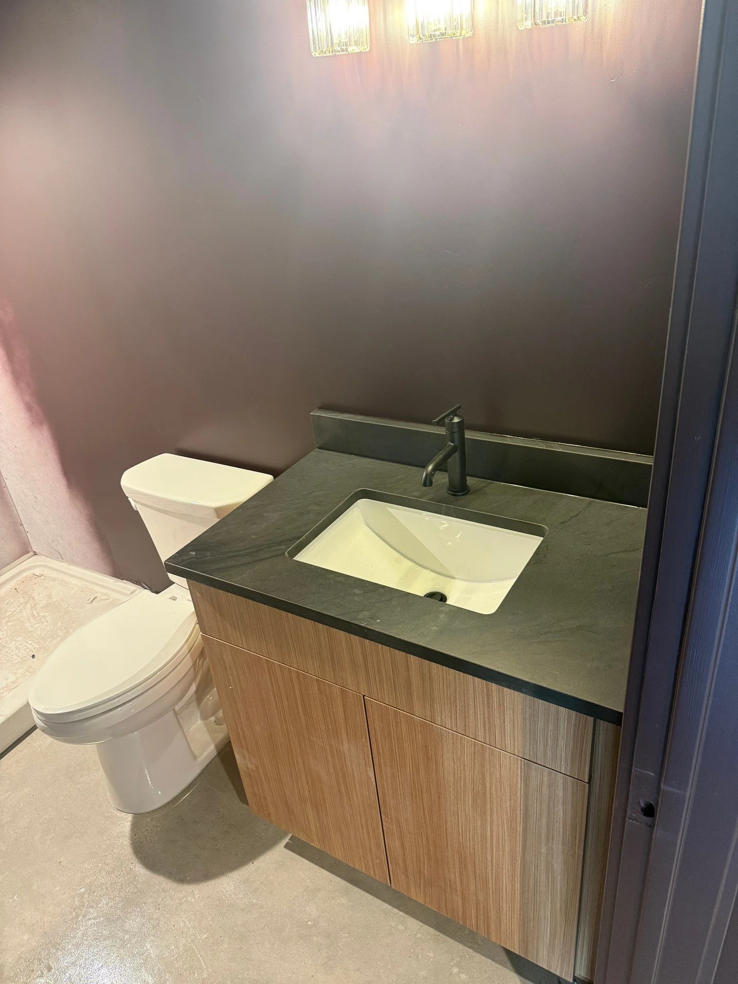 Clean, straightforward bathroom finish today. New toilet set on the finished floor, and a wall-mounted vanity with an integrated sink and countertop faucet. Supply lines and drain are tucked neatly inside the cabinet for a simple, tidy look. Everyday