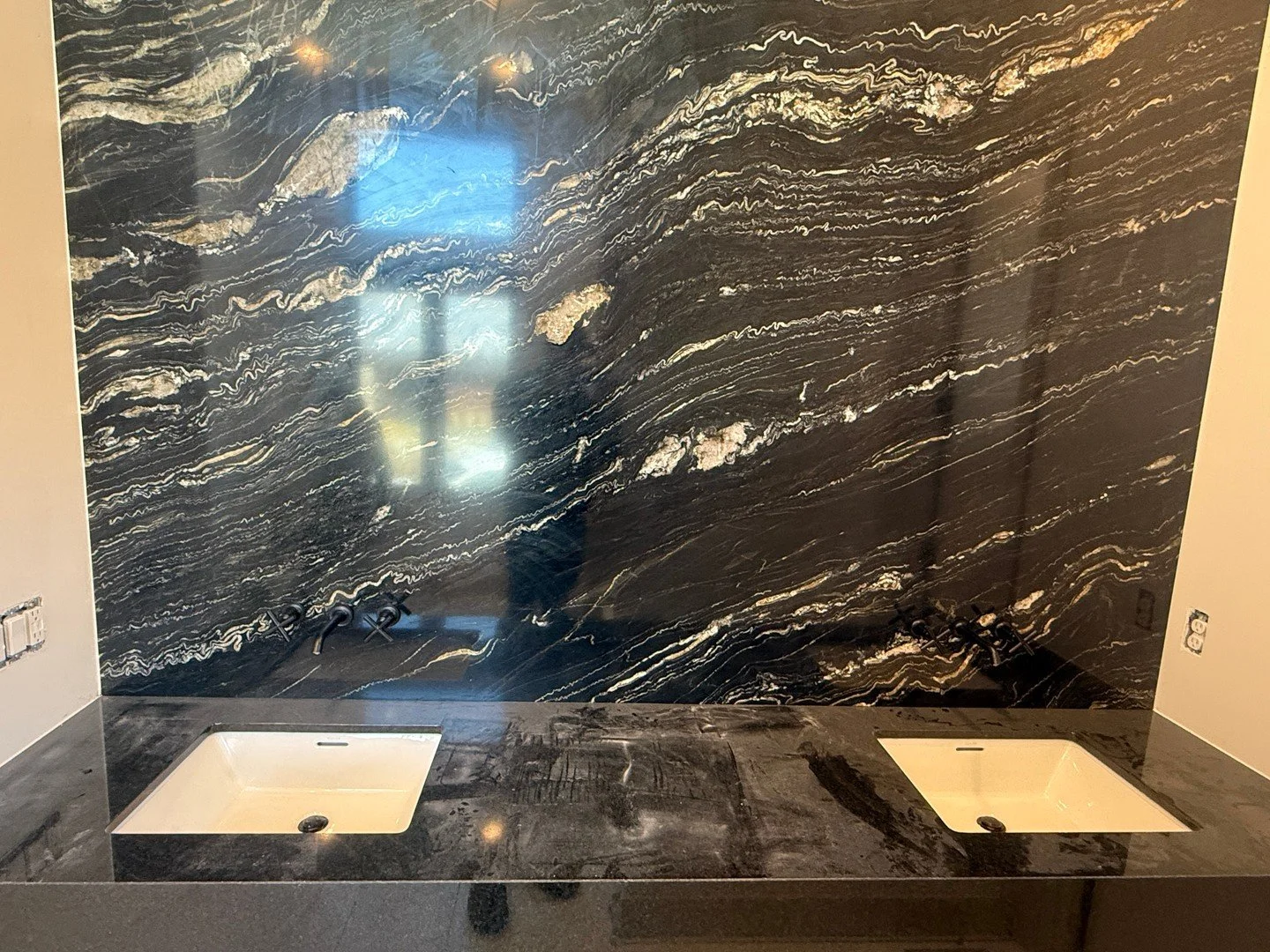 Details first on this double vanity. Rough-in is dialed and the wall-mounted faucet valves are lined up right above the under-mount rectangles, with the stone top and backsplash set clean. Trim and handles go on at the finish, but the groundwork is d