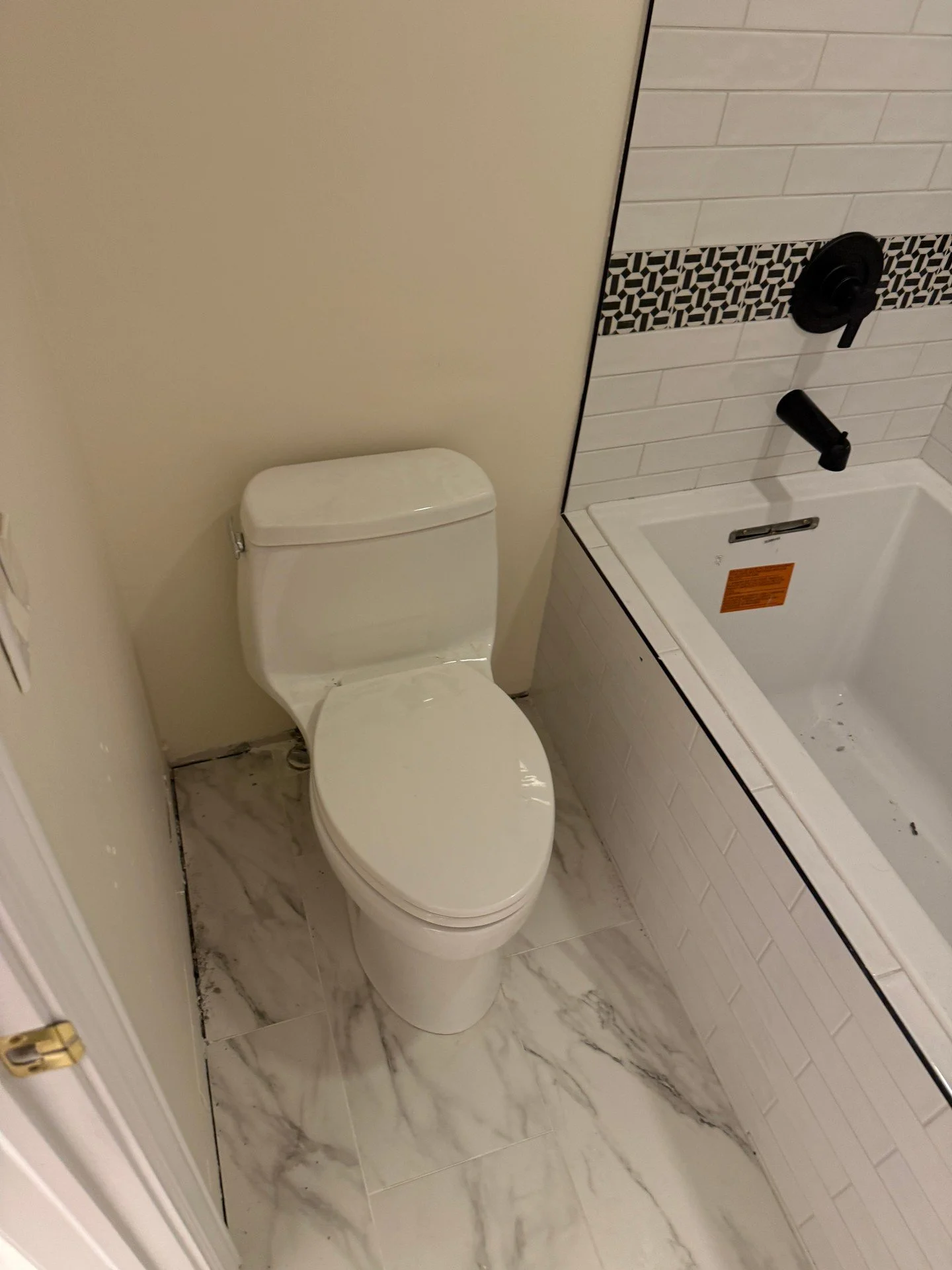 Toilet set on tile and supply hooked up, with the tub/shower trim in place next door. Plumbing and tile are wrapped up; caulk and baseboards will finish it off. Clean lines and tight connections&mdash;right where they should be. Another steady day of