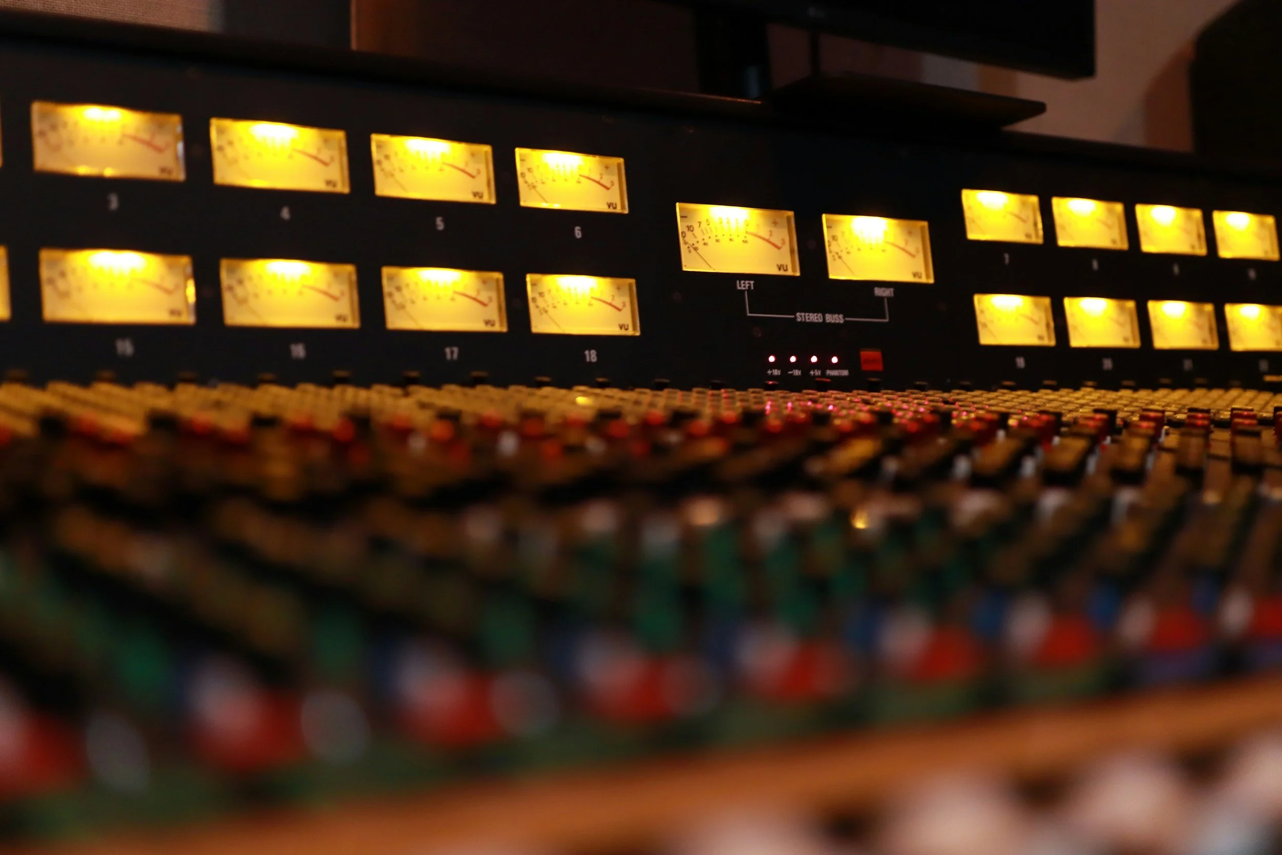 A close-up view of a vintage audio mixing console with illuminated VU meters and numerous control knobs.
