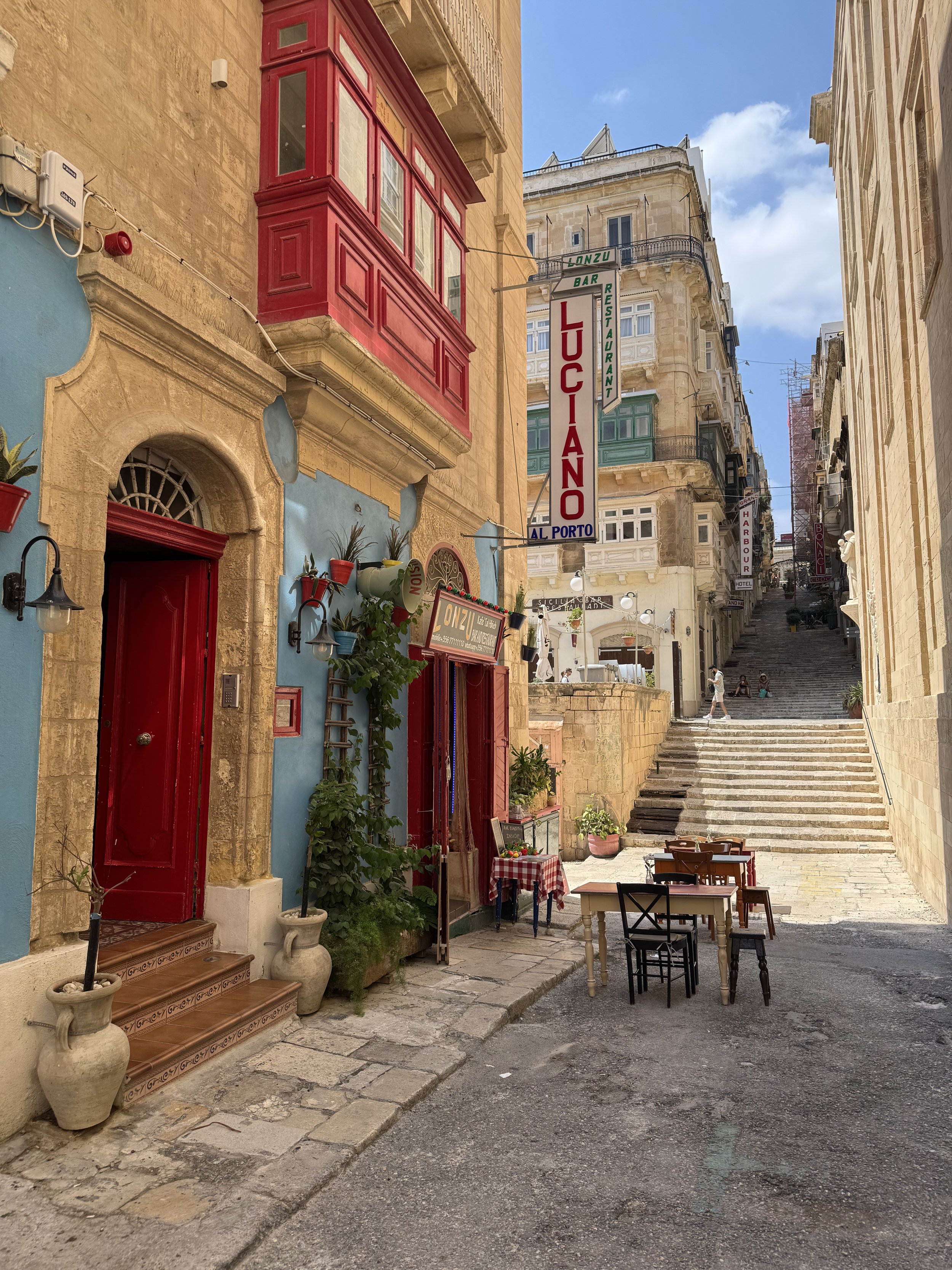 Colorful street scene with restaurant signs, outdoor tables, and stone stairs leading upward in a European city with historic architecture.