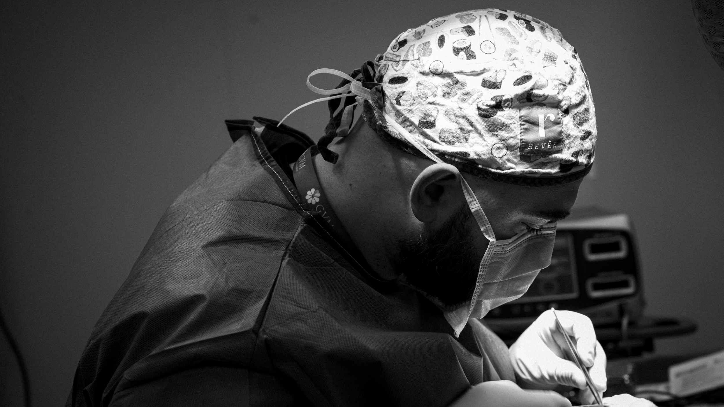 Un chirurgo in sala operatoria si sta preparando, indossa una maschera e un cappello chirurgico con disegni, mentre si concentra sul suo lavoro.