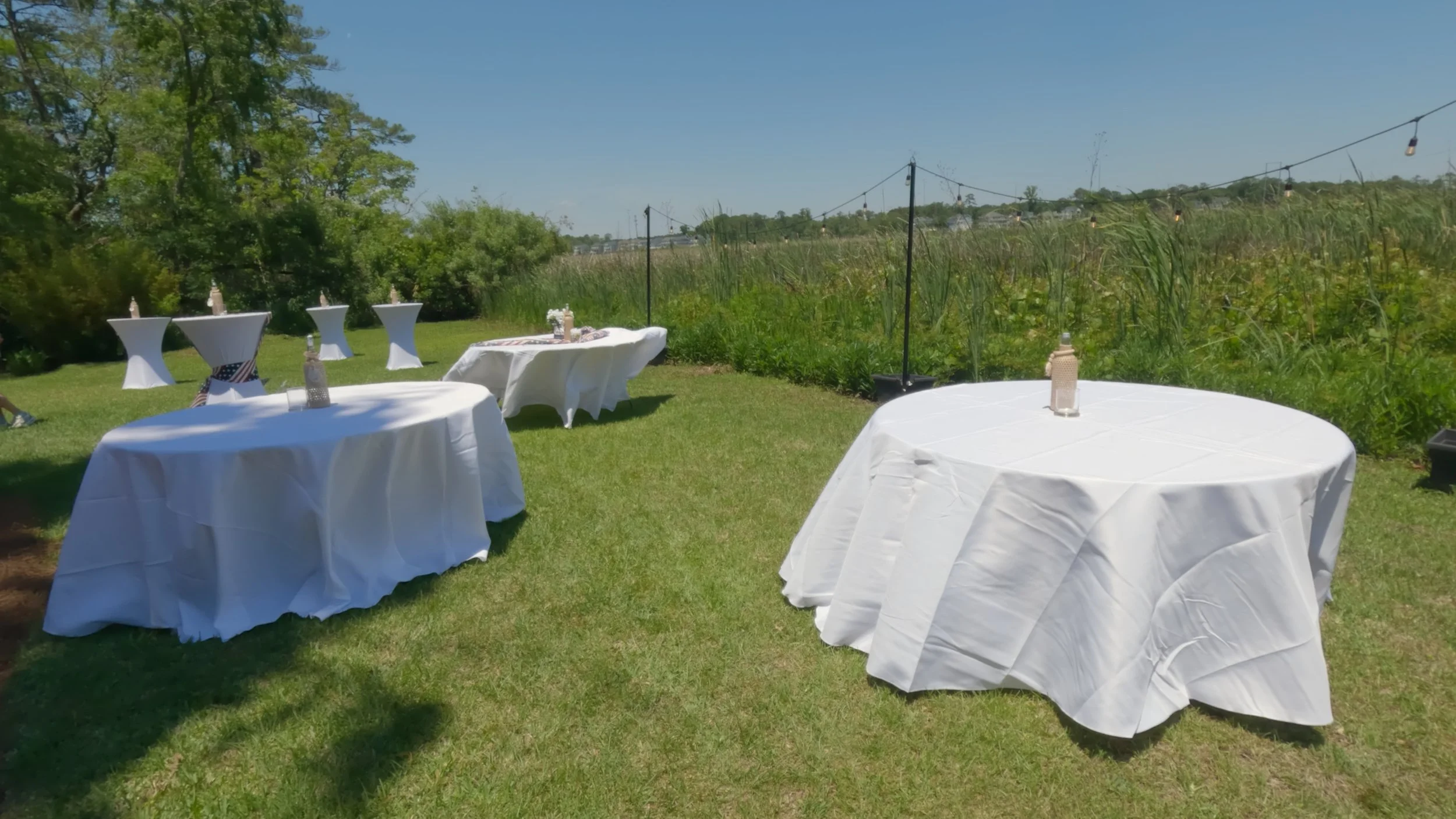 Outdoor event setup with white event rental chairs round tables covered in white tablecloths, in South Carolina